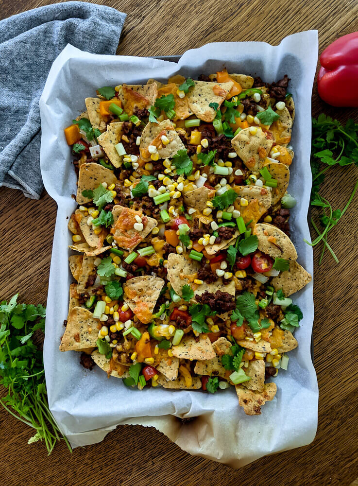 Sheet Pan Nachos on a baking tray resting on a table, sprinkled with cilantro.