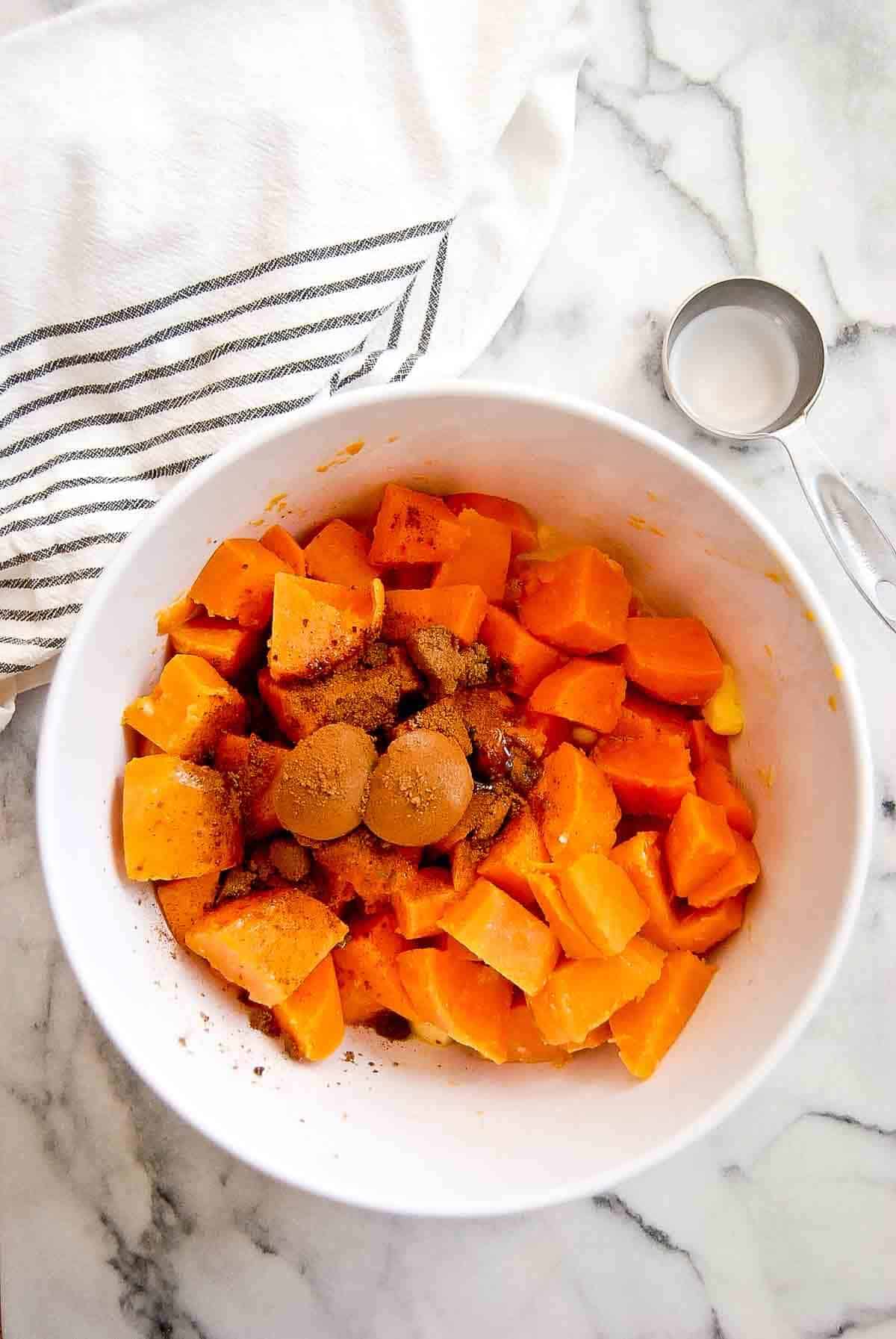 cooked chopped sweet potatoes in bowl with brown sugar and cinnamon.