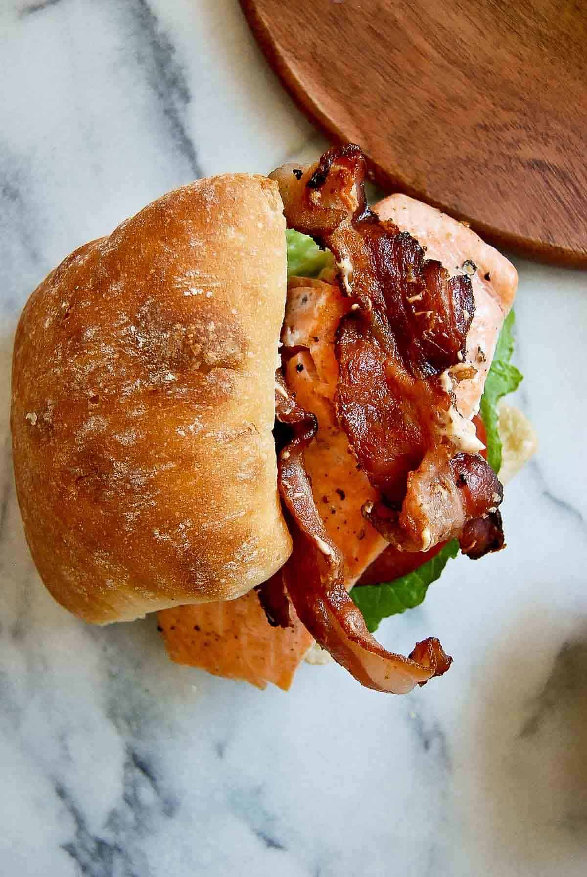 salmon blt sandwich on cutting board.