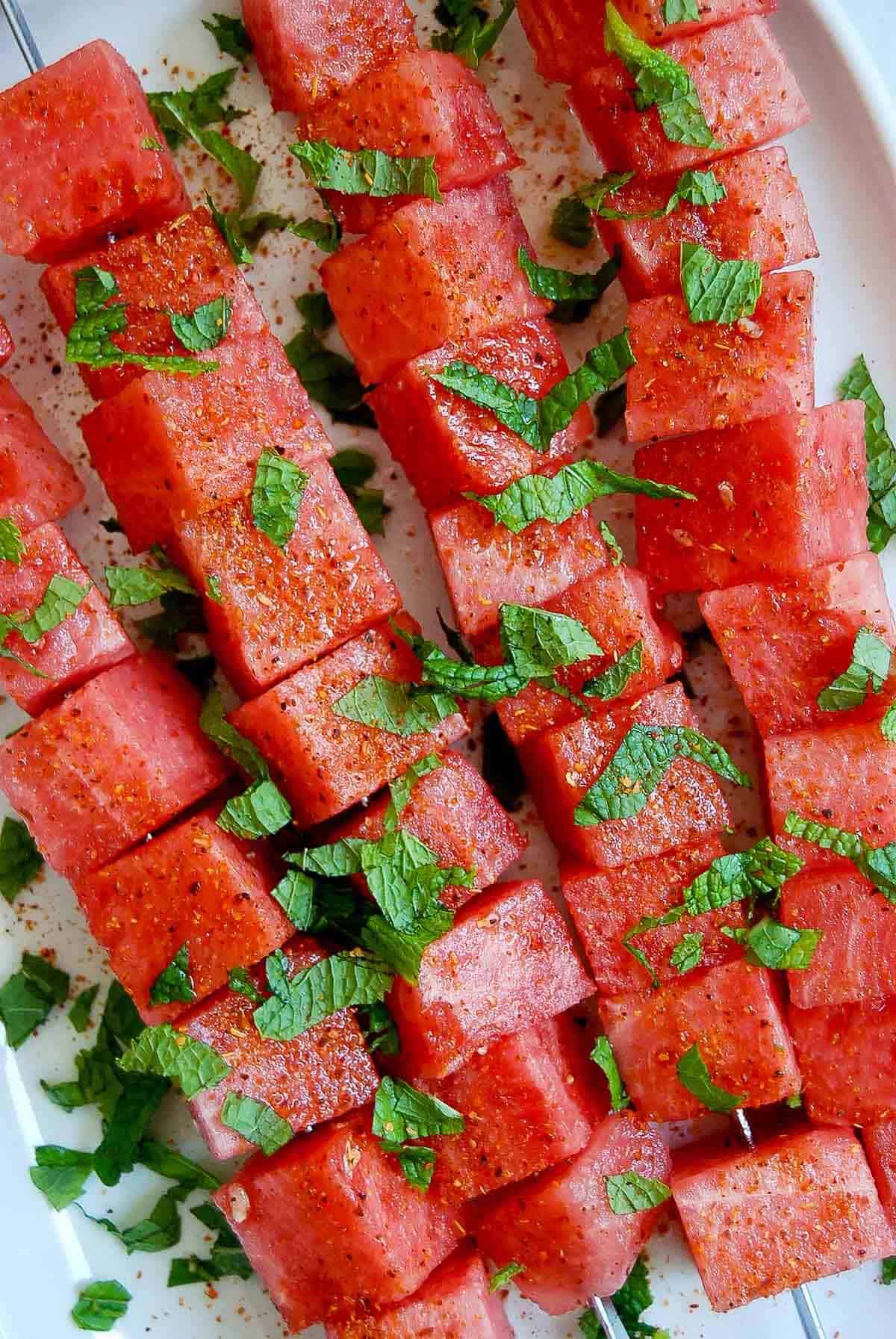 closeup of watermelon with tajin, lime and mint on plate.