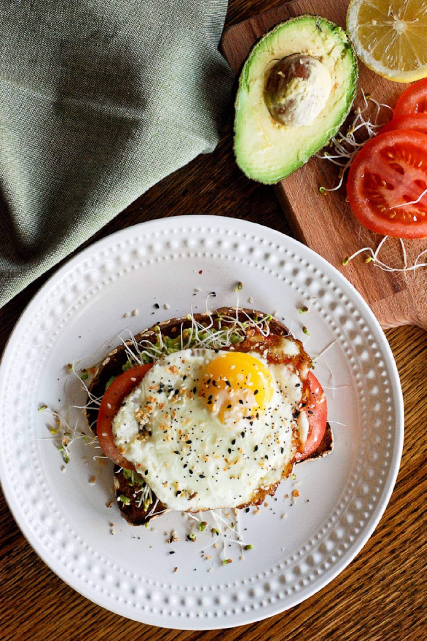 avocado toast with fried egg and tomato on plate.