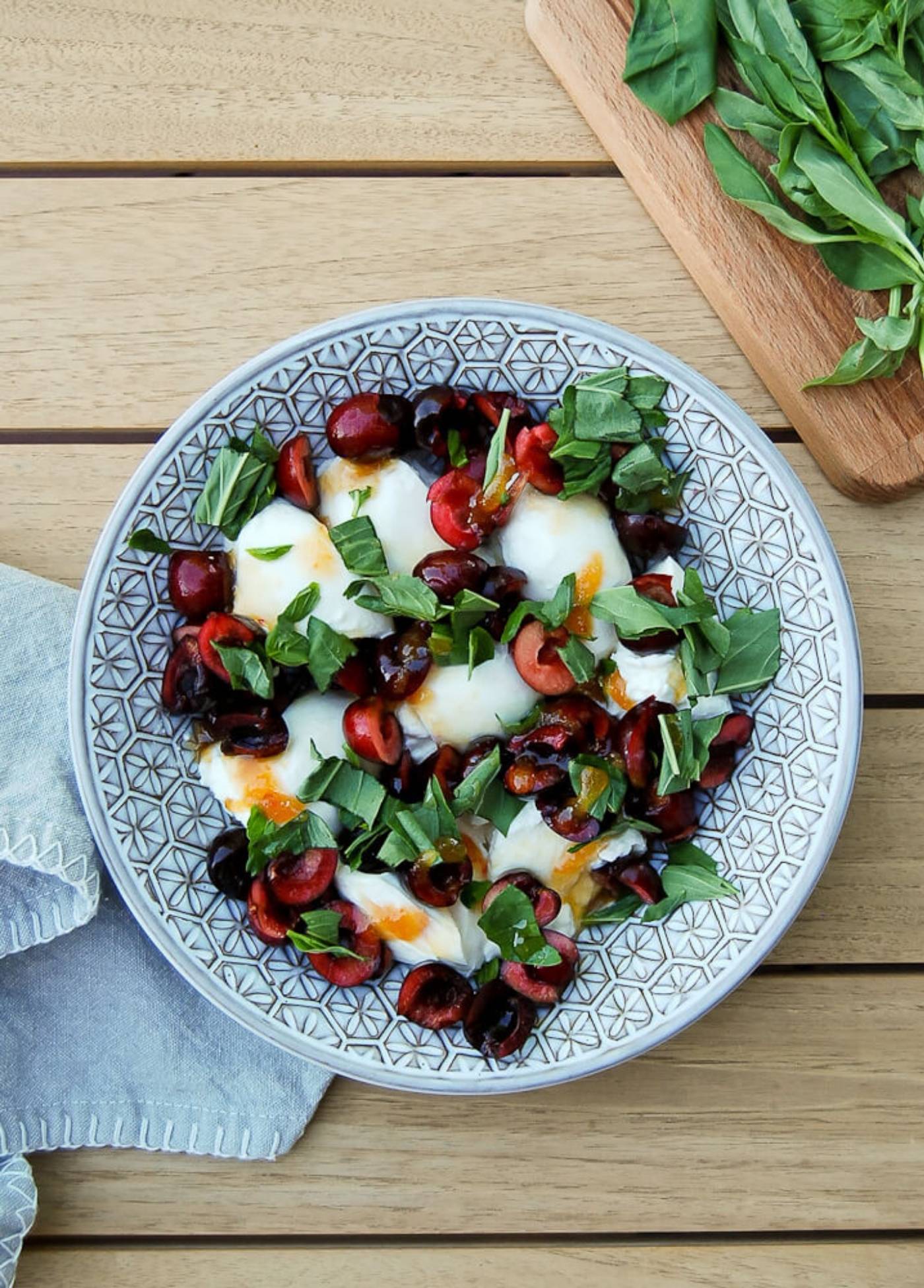 Burrata, cherry, hot honey and basil salad in bowl on table.