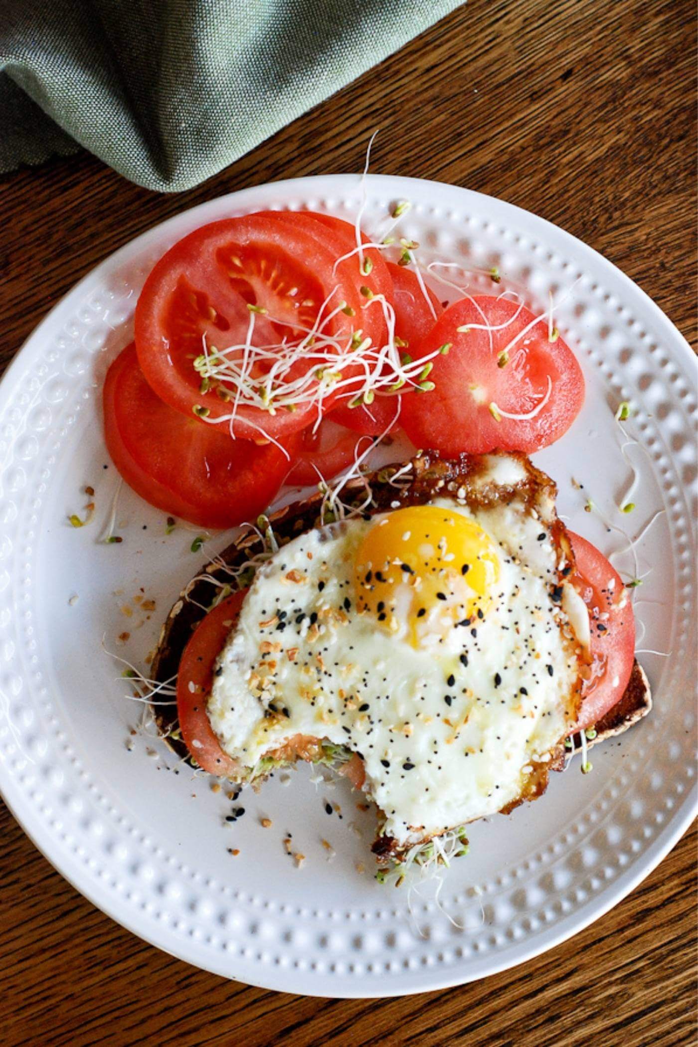 Avocado with fried egg and tomato on plate.