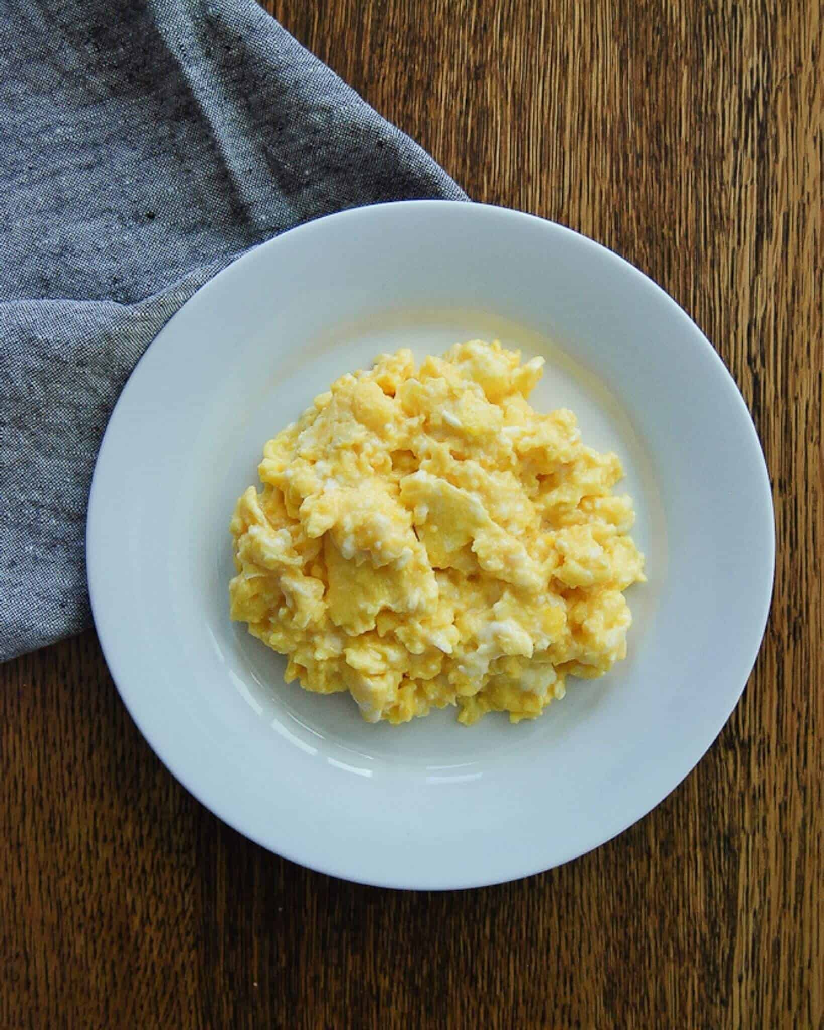 Scrambled eggs on plate with napkin on the side.