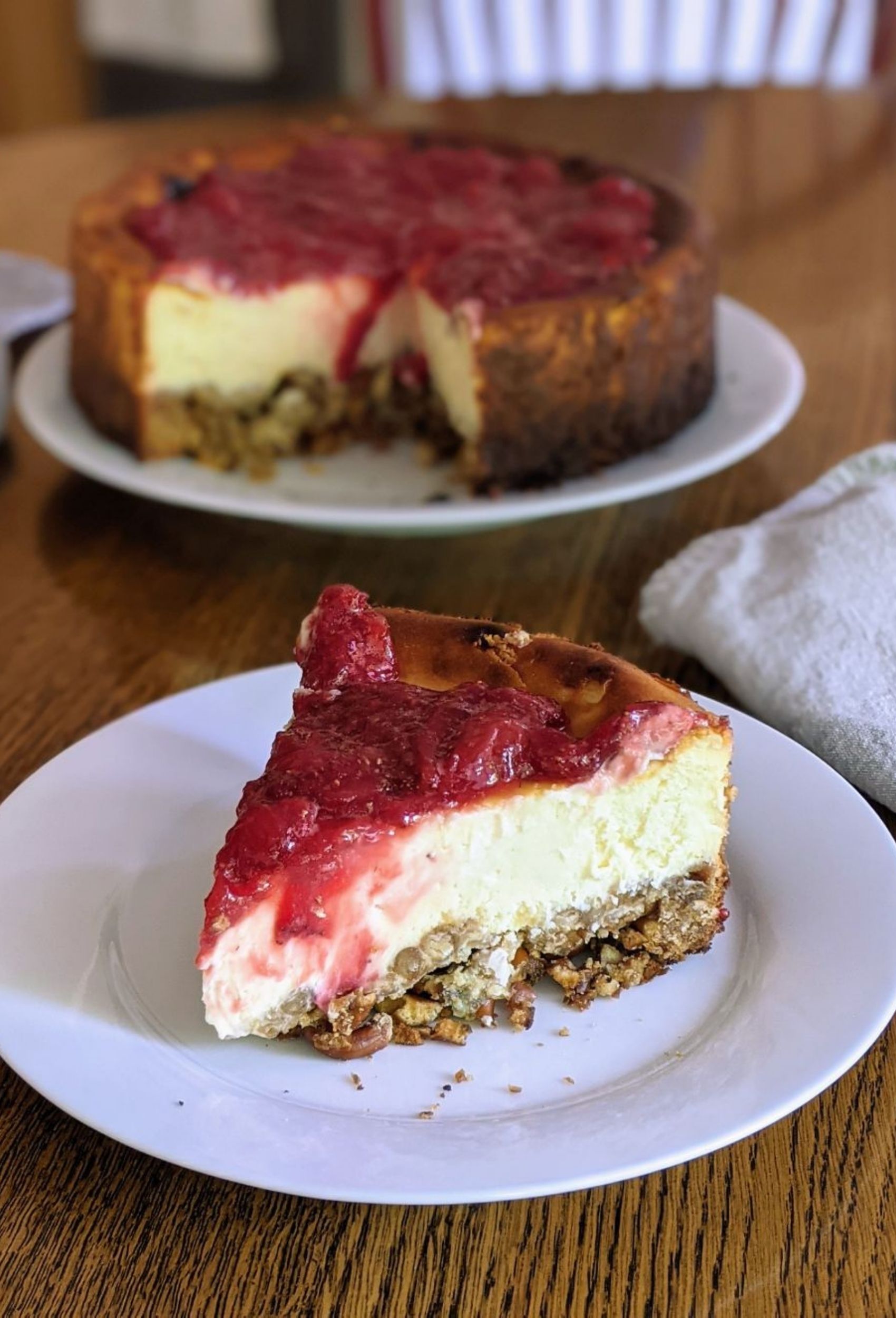 Slice of strawberry cheesecake with a pretzel crust, with full cheesecake in the background.