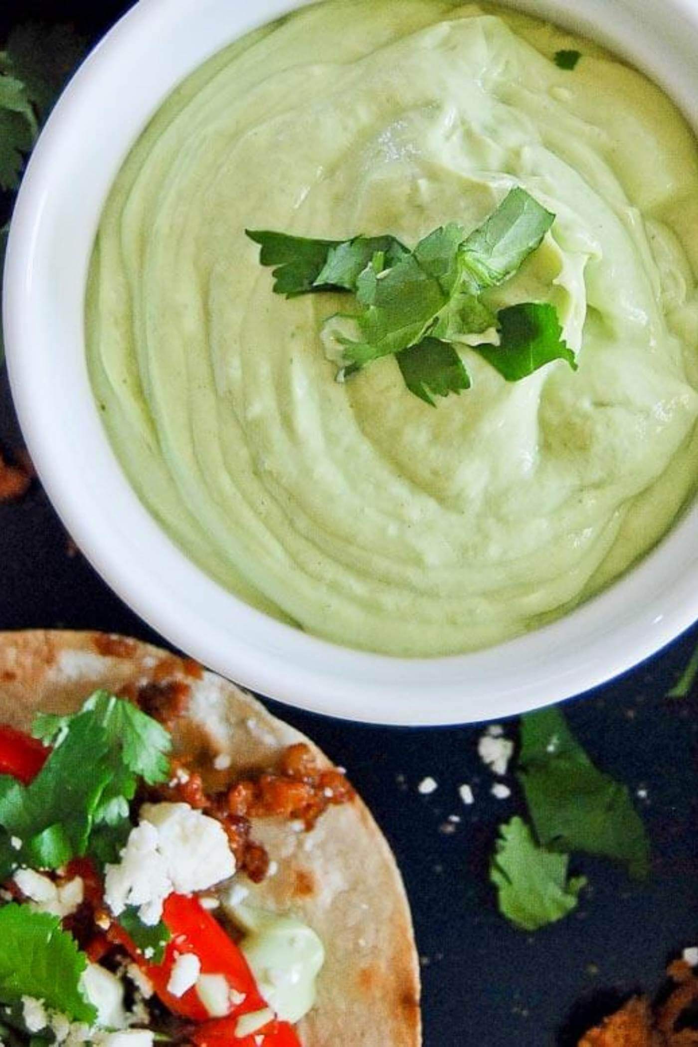 avocado lime sauce in bowl next to chorizo and red pepper tostada.