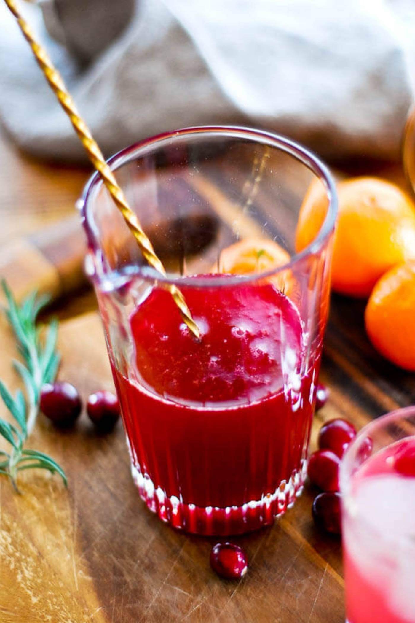 cranberry orange and rosemary shrub syrup in glass with stirrer.