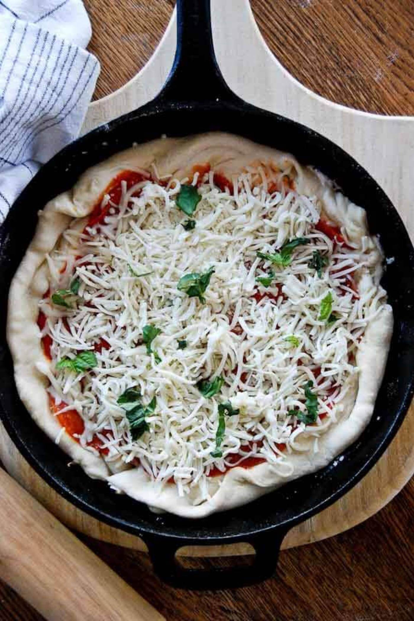 cast iron skillet pizza ready for baking, topped with mozzarella cheese and basil.