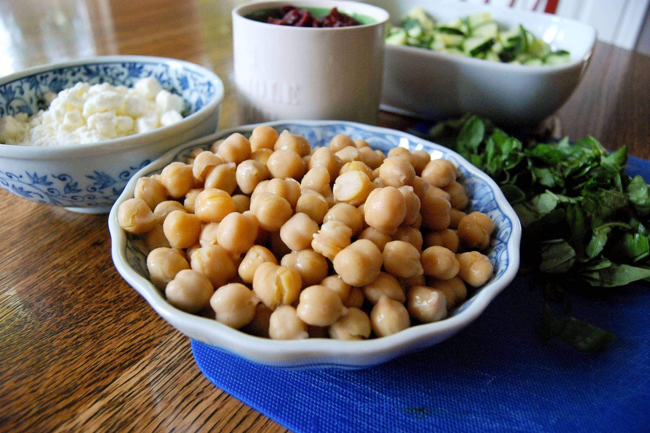 bowl of chickpeas on table surrounded by other salad ingredients.