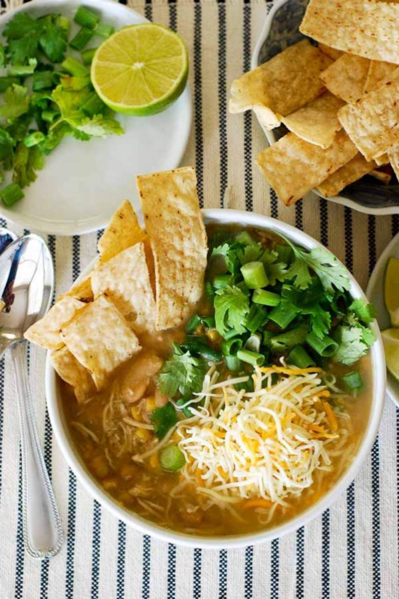 chicken chili in bowl with cheese, onions and chips.