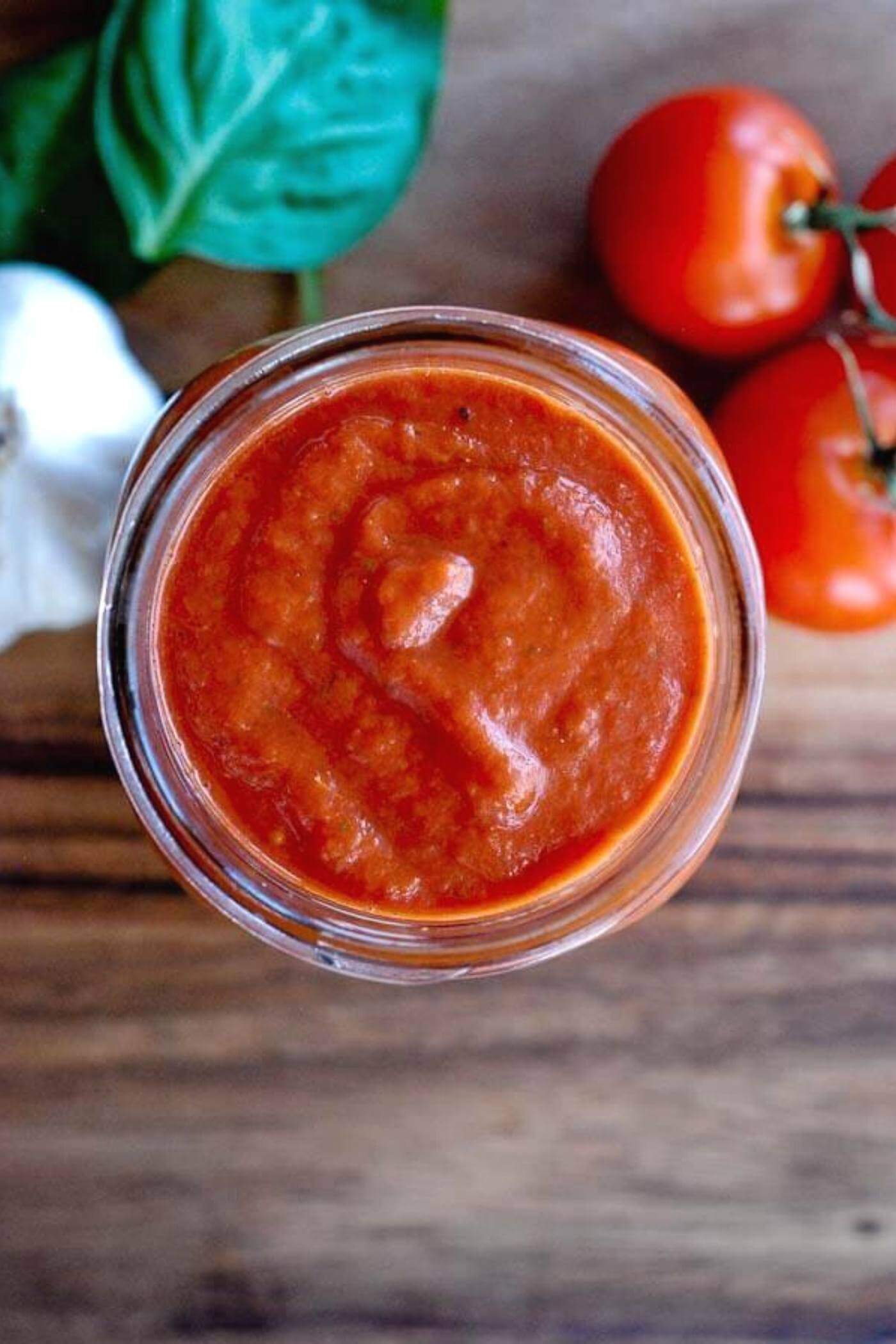 easy homemade pizza sauce in jar surrounded by tomatoes, garlic and basil.