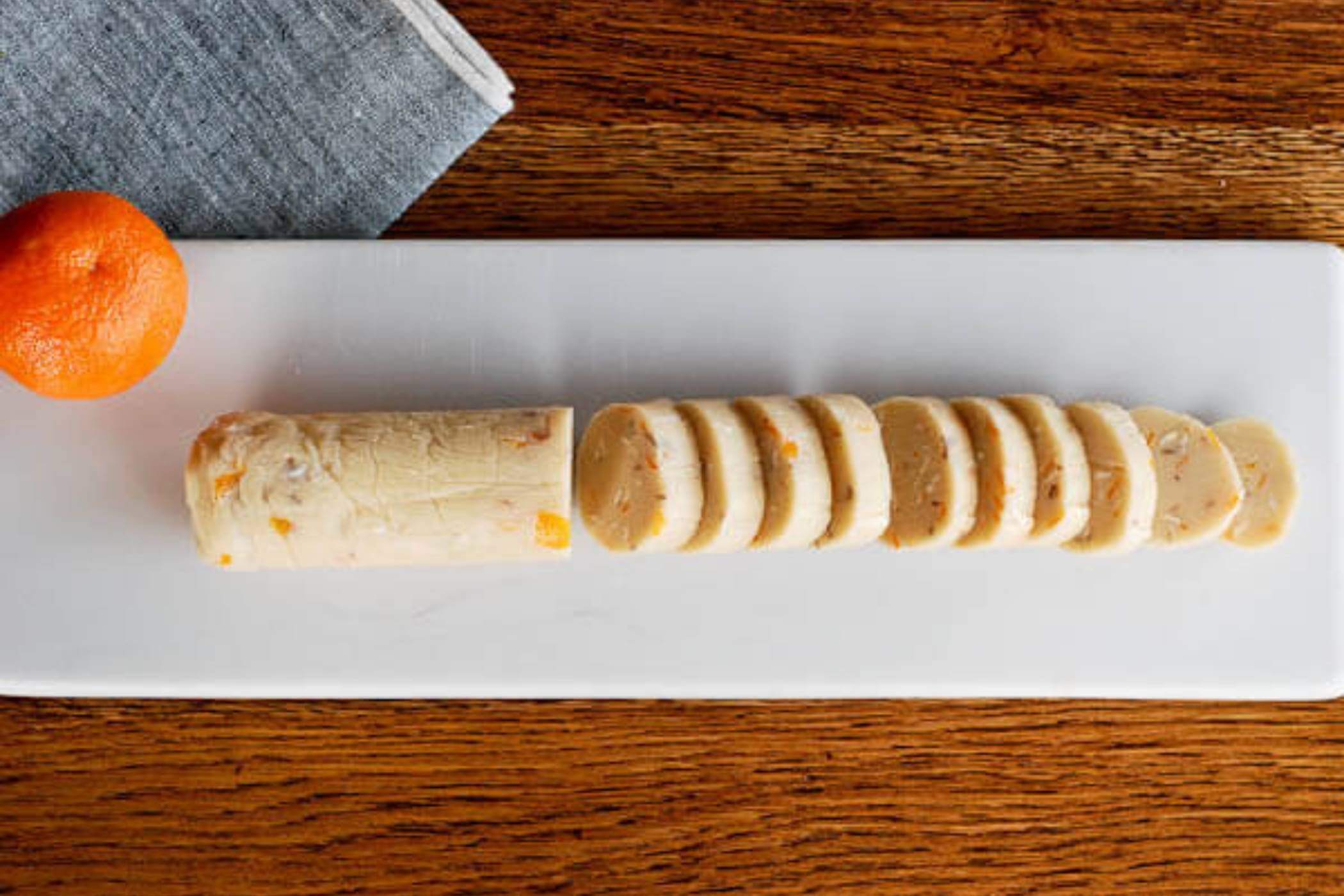 orange and almond shortbread cookie in roll, sliced on cutting board.