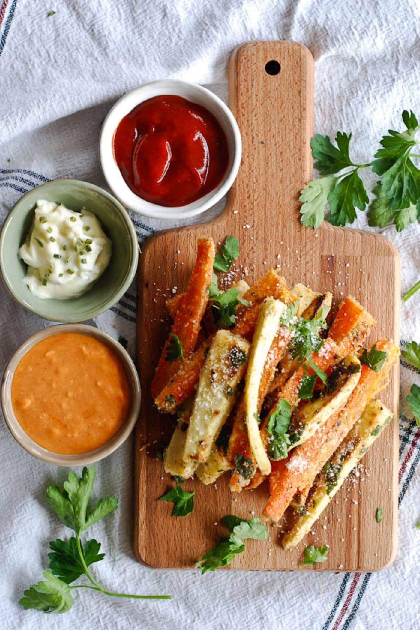 baked parmesan carrot and parsnip fries on cutting board with sauces