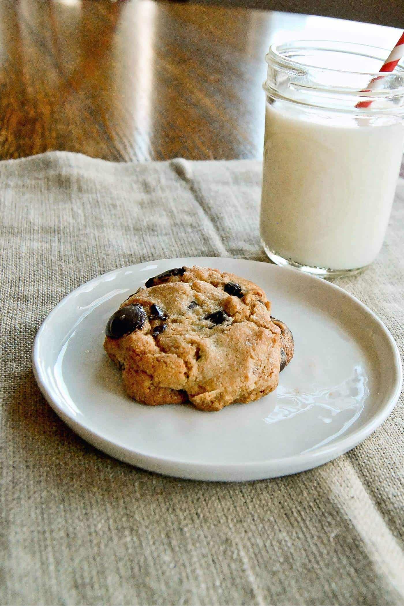 chocolate chip cookie on plate with milk in background.