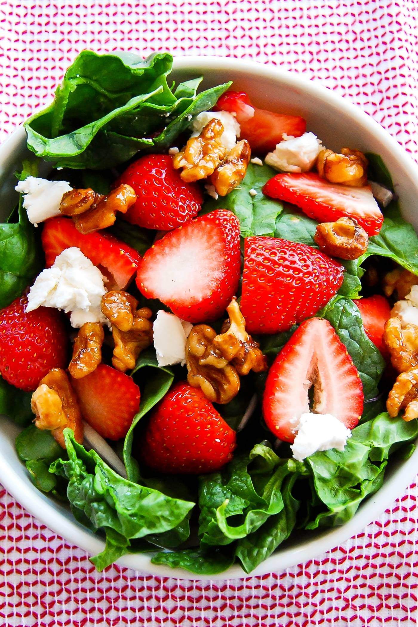 spinach and strawberry salad with goat cheese and candied walnuts in bowl.