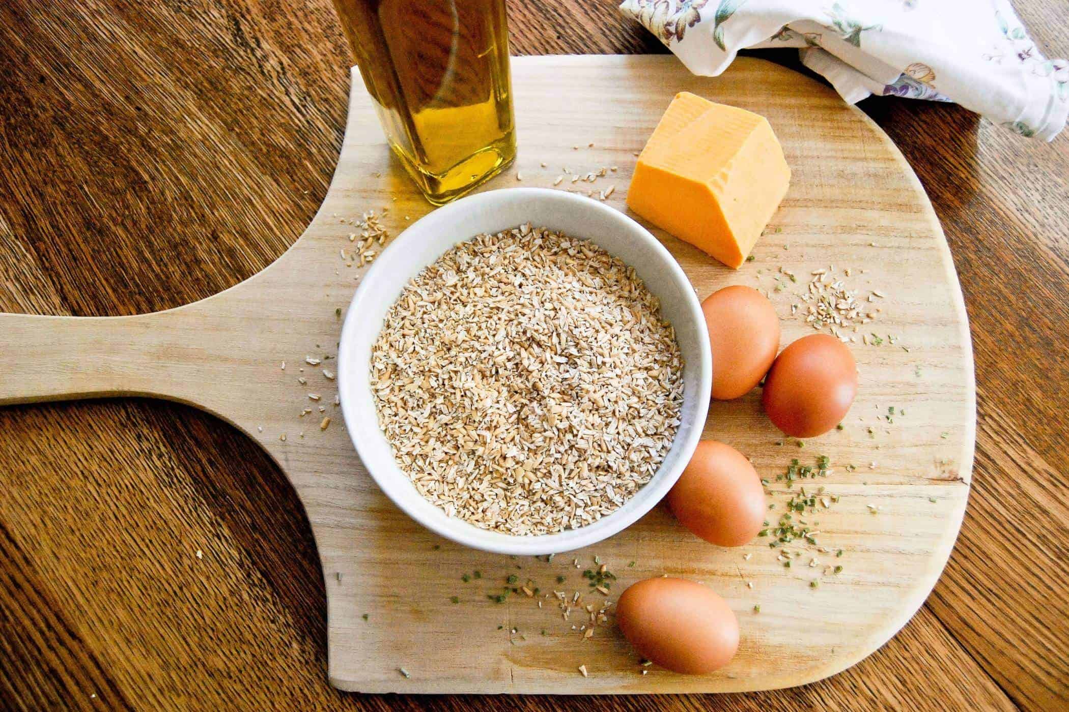 steel cut oats in bowl with whole eggs and block of cheese on cutting board.