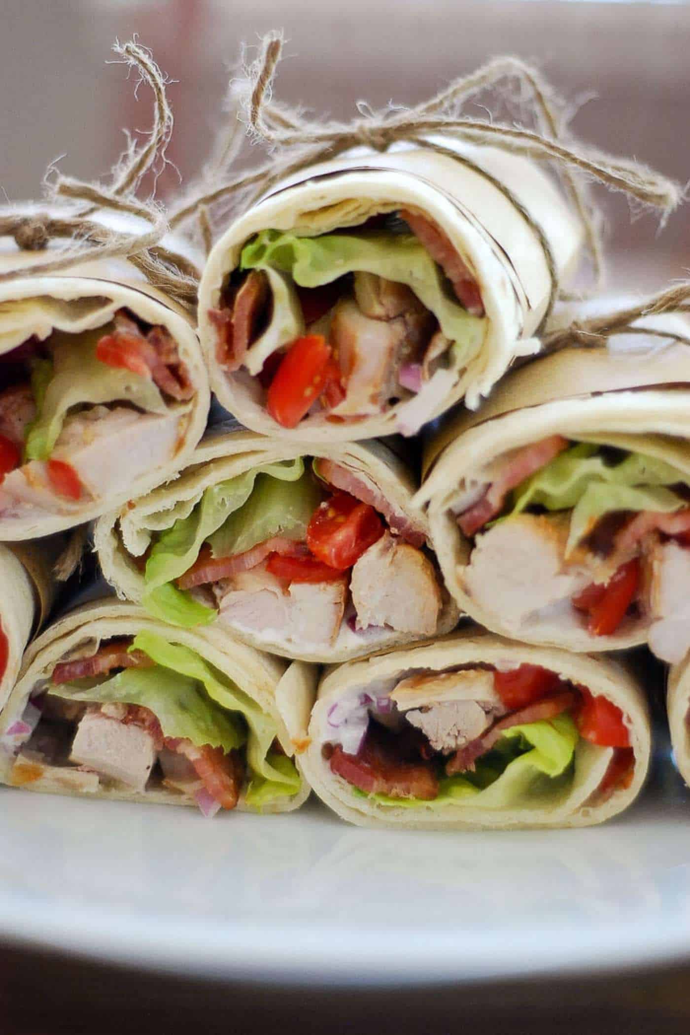 chicken bacon ranch wraps stacked on a plate, tied with paper and string.