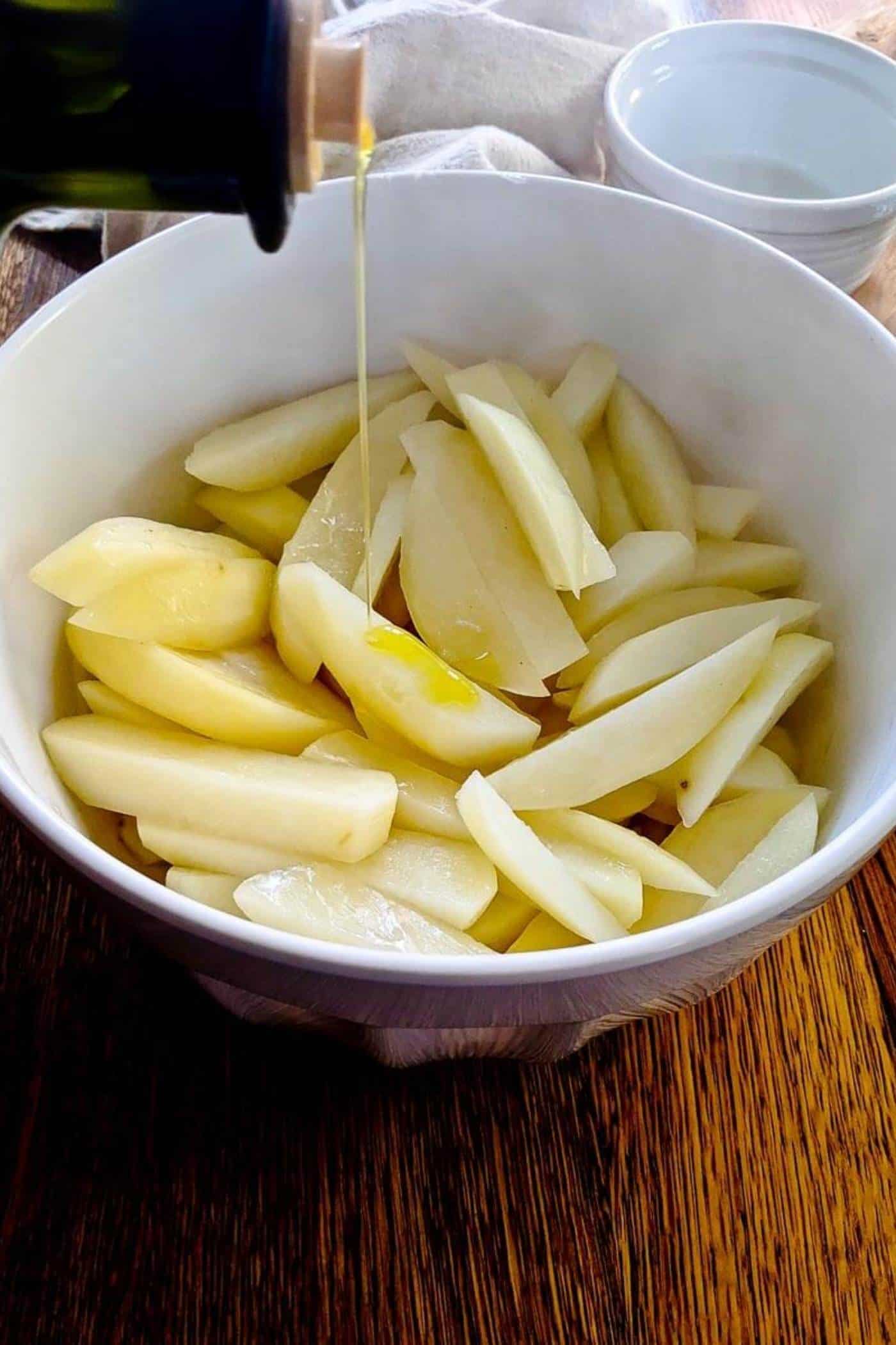 steamed potato fries in a bowl, being drizzled with oil.