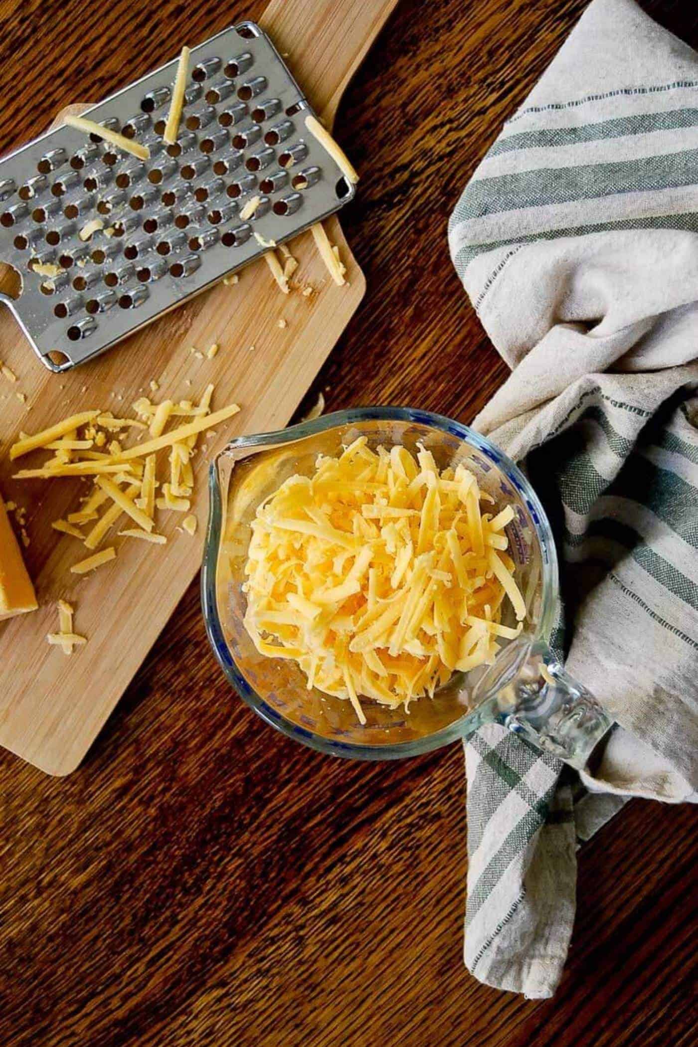 2 cups of shredded cheddar cheese, next to cheese grater.