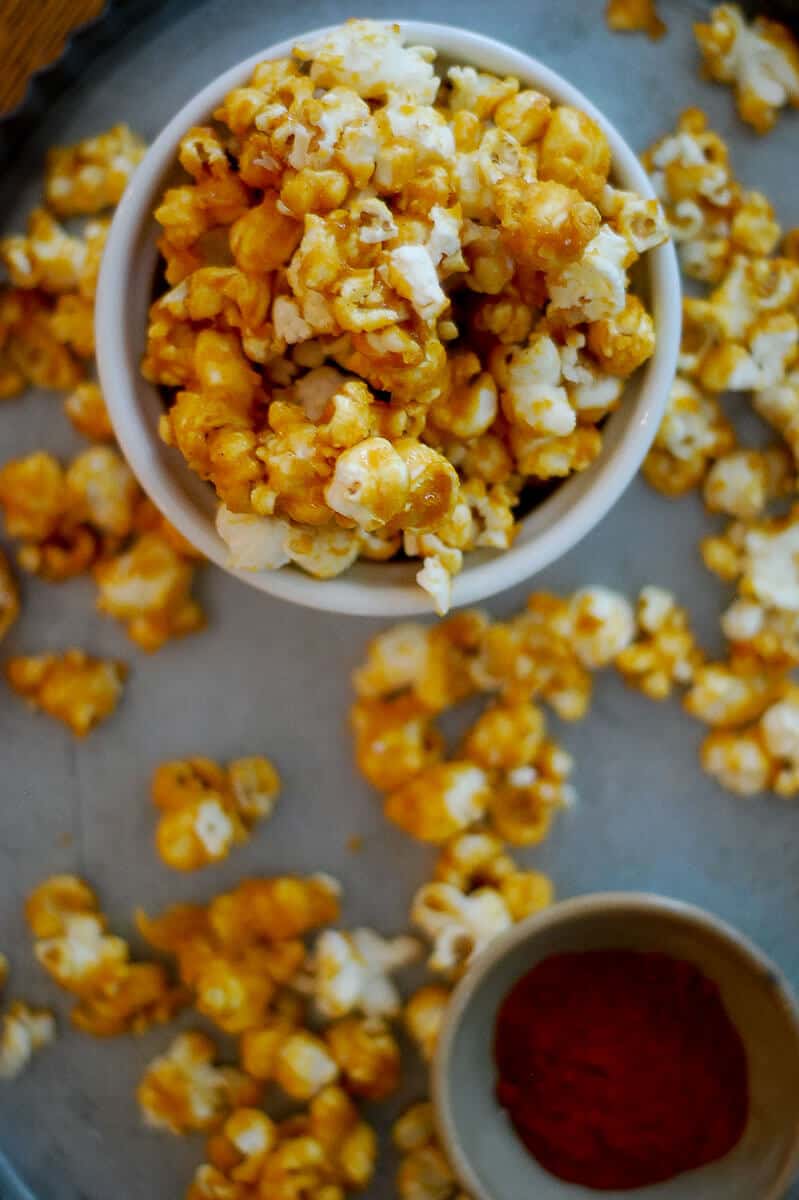 spicy caramel popcorn in bowl with scattered kernels around bowl.