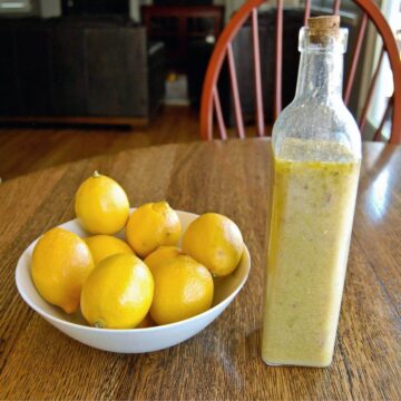 lemon rosemary vinaigrette dressing in bottle next to bowl of lemons.