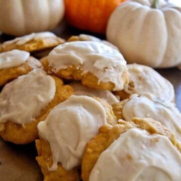 pumpkin cookies with cream cheese icing stacked on tray.