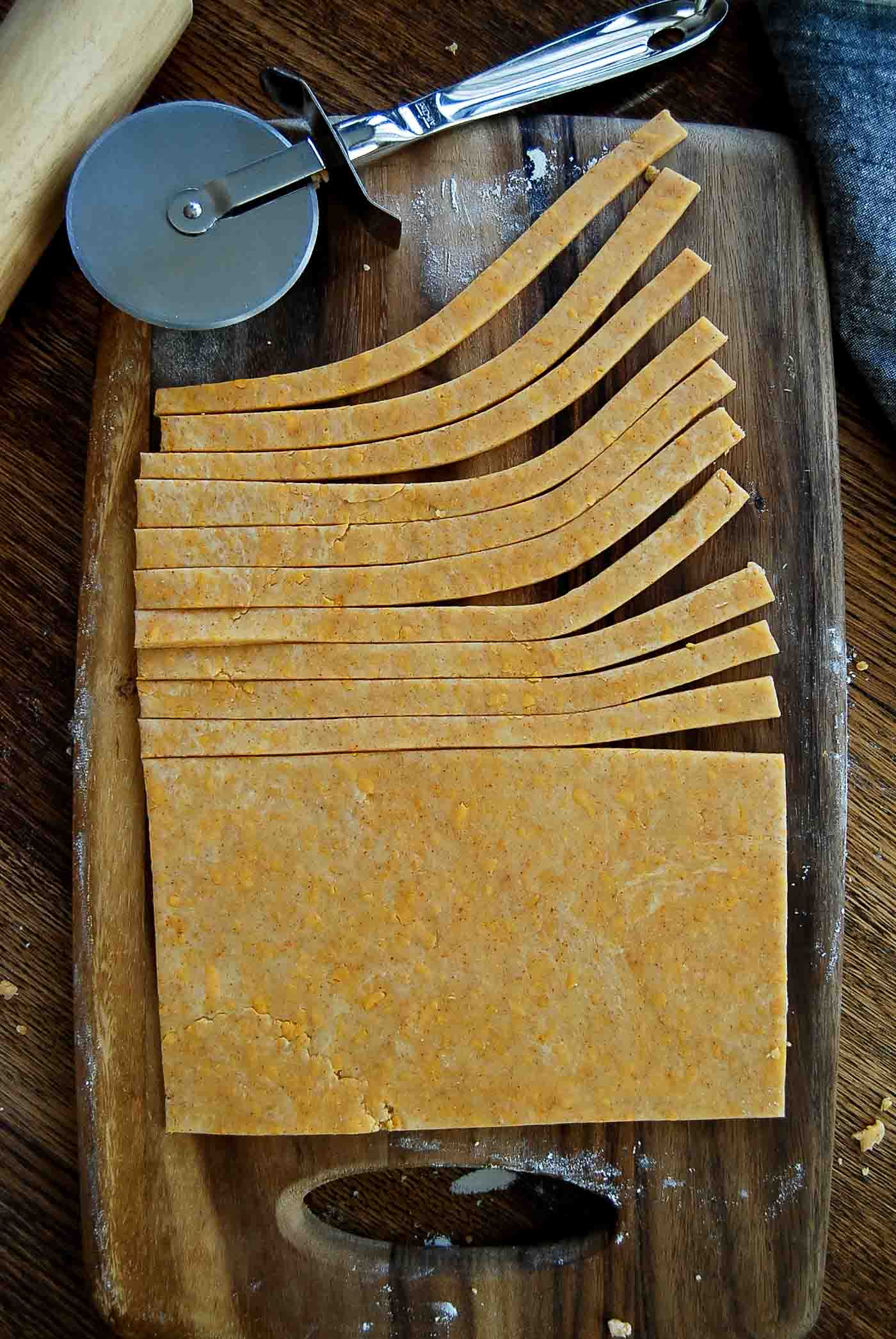 cheddar cheese dough being cut into cheese straws.