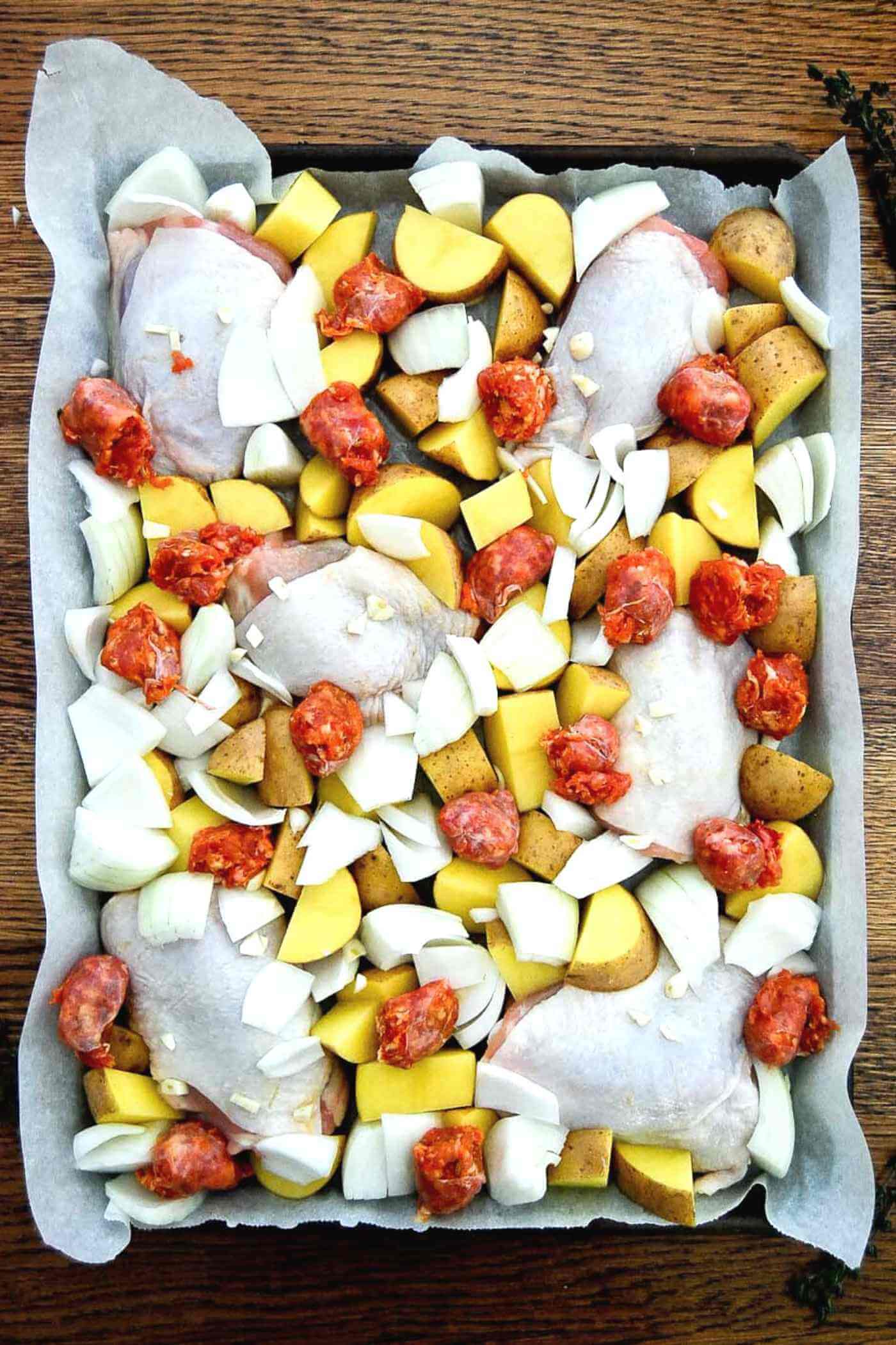 chicken thighs, potatoes, onion and sausage on sheet pan.