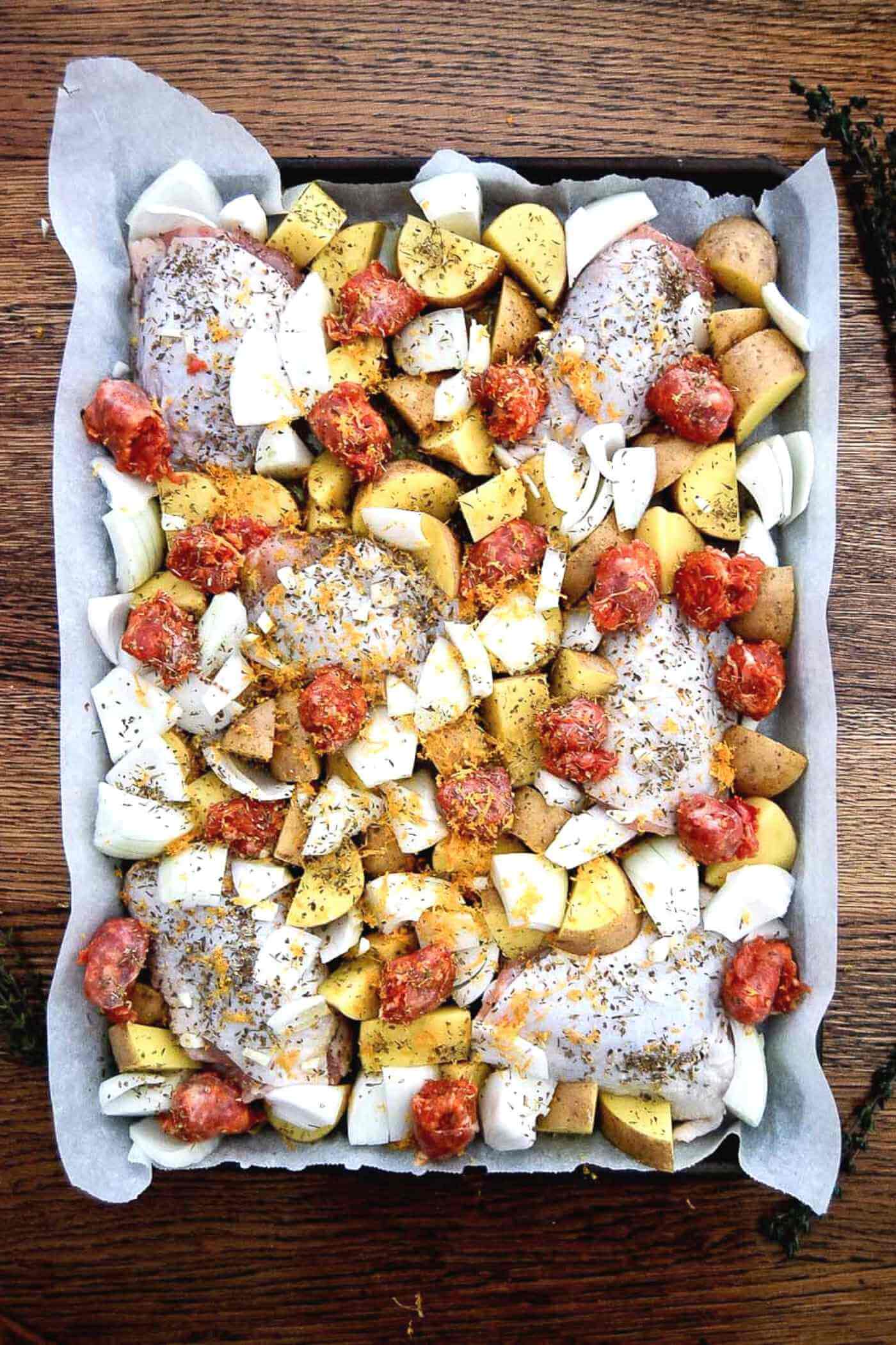 sheet pan chicken thighs with sausage and potatoes before baking.