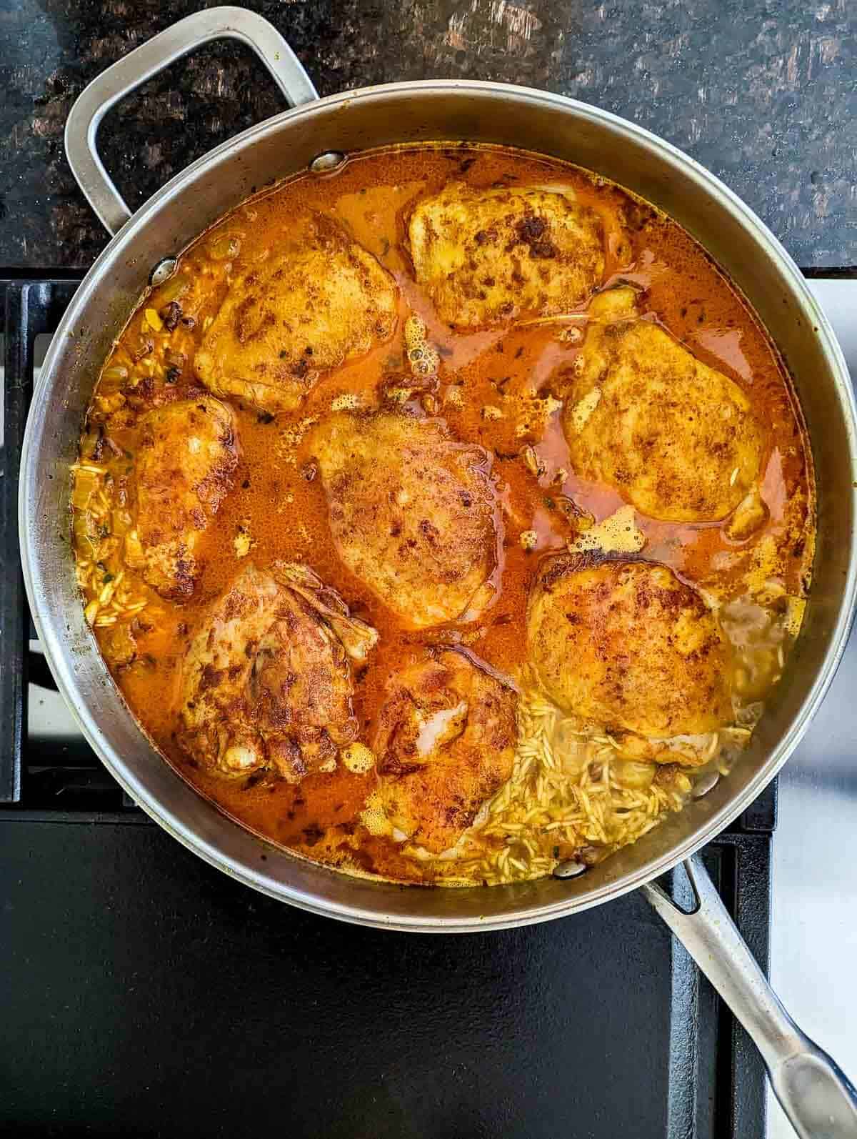 seared chicken thighs and yellow rice simmering in broth in a pan on the stovetop.