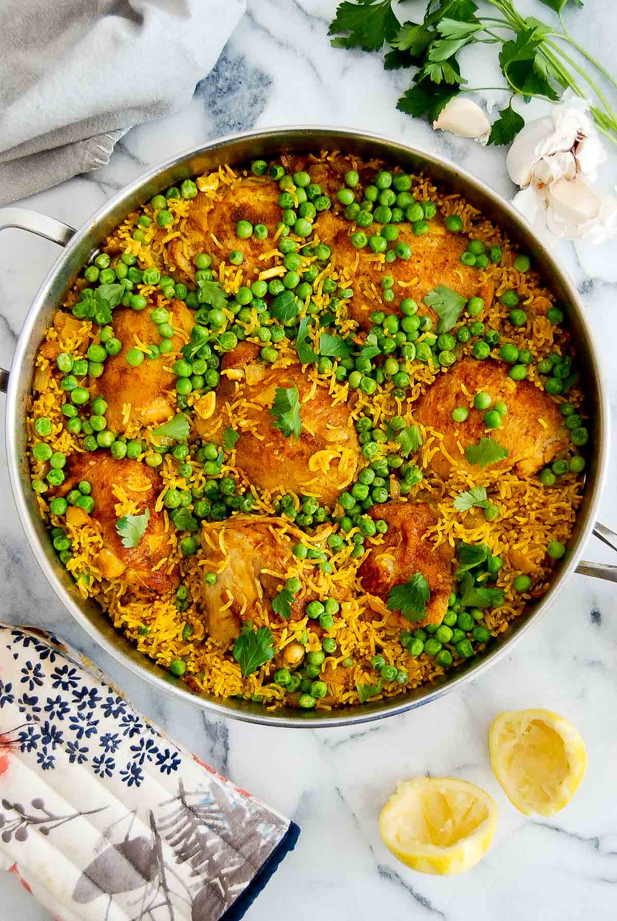 yellow chicken and rice with peas in pan on cutting board with garlic, parsley and lemon peel on the side.