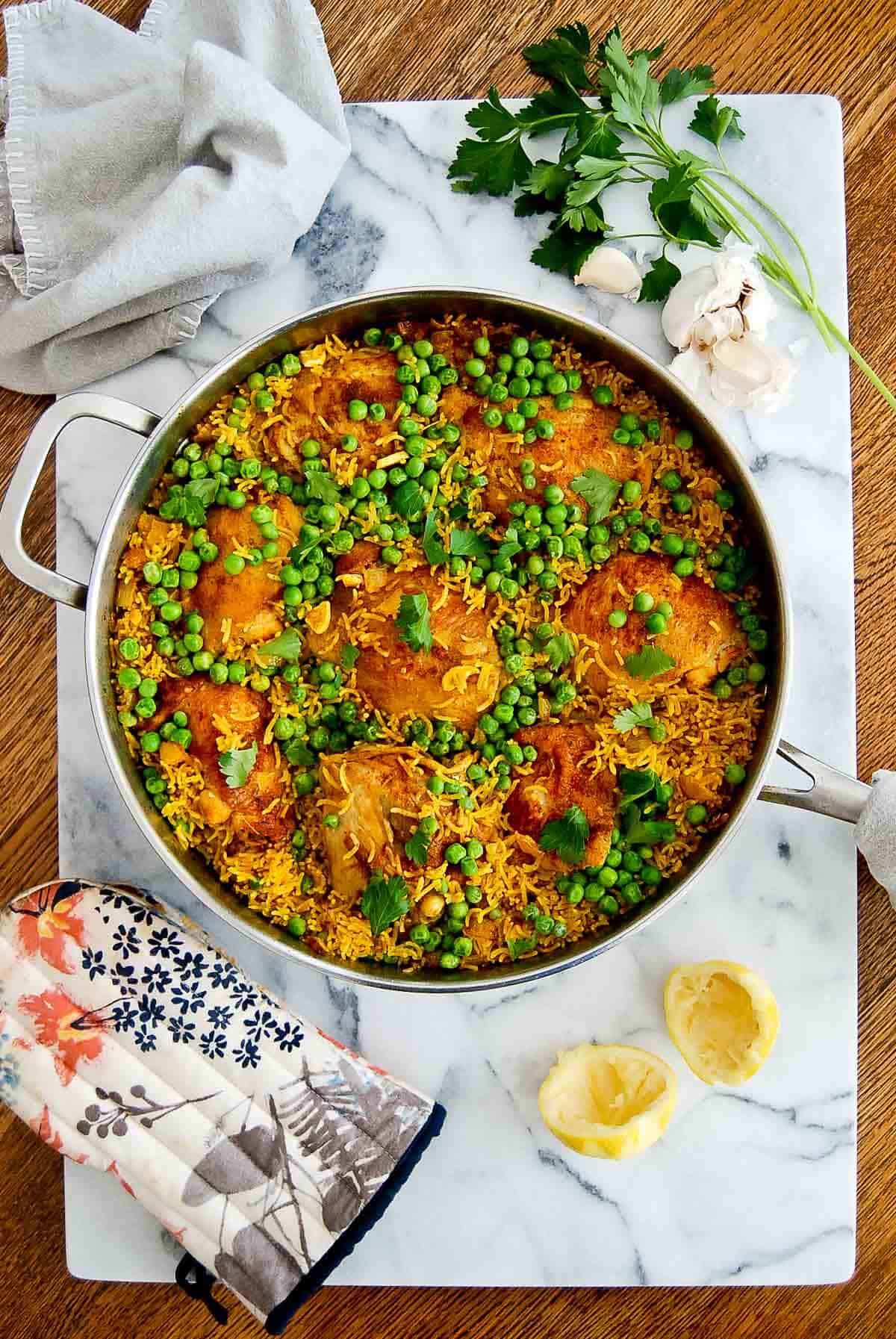 chicken and yellow rice with peas on cutting board with garlic, parsley and lemon peel on the side.