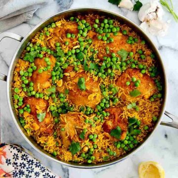 chicken and yellow rice with peas in pan with garlic, parsley and lemon peel on the side.