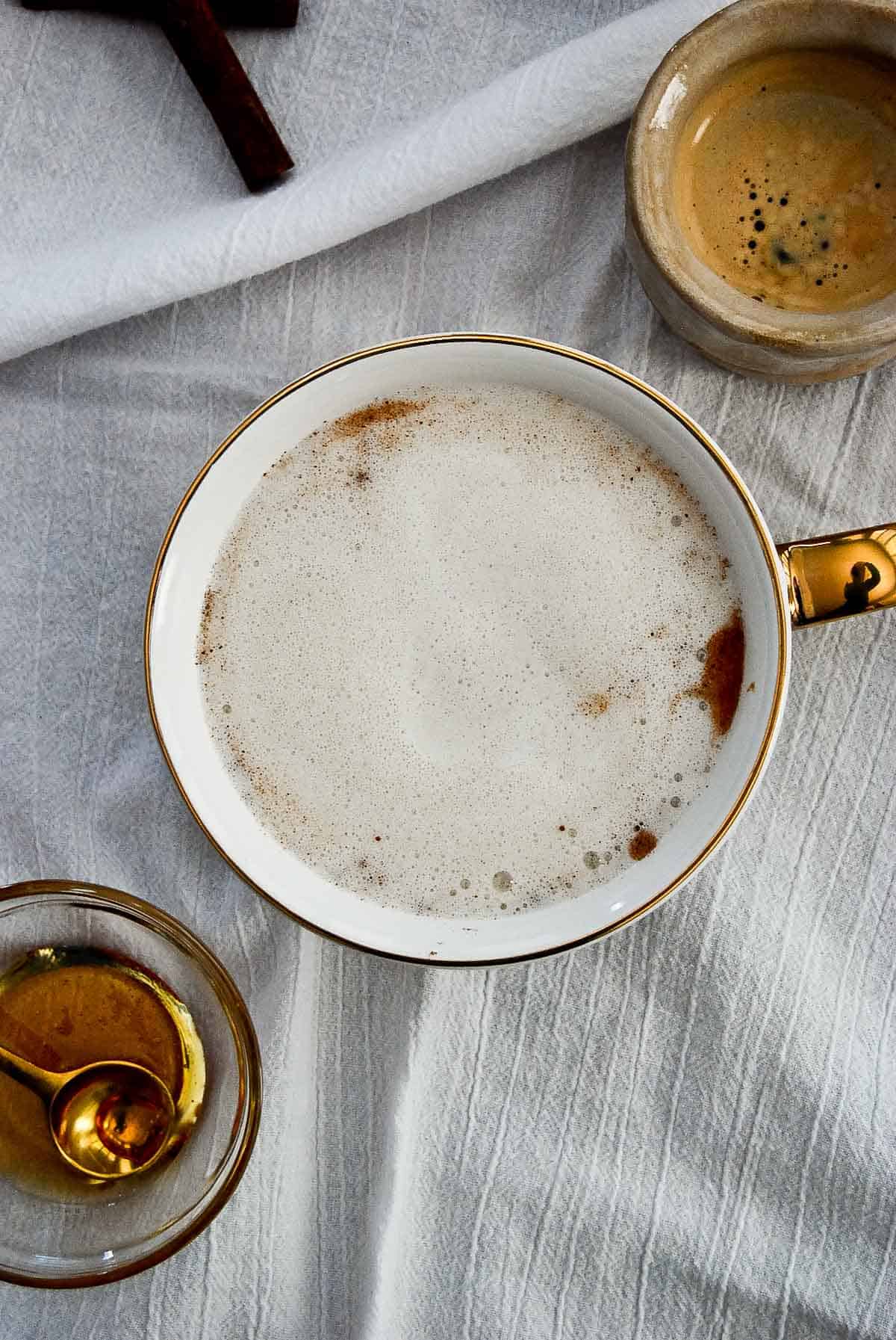 Mug with steamed milk, honey and cinnamon on napkin.