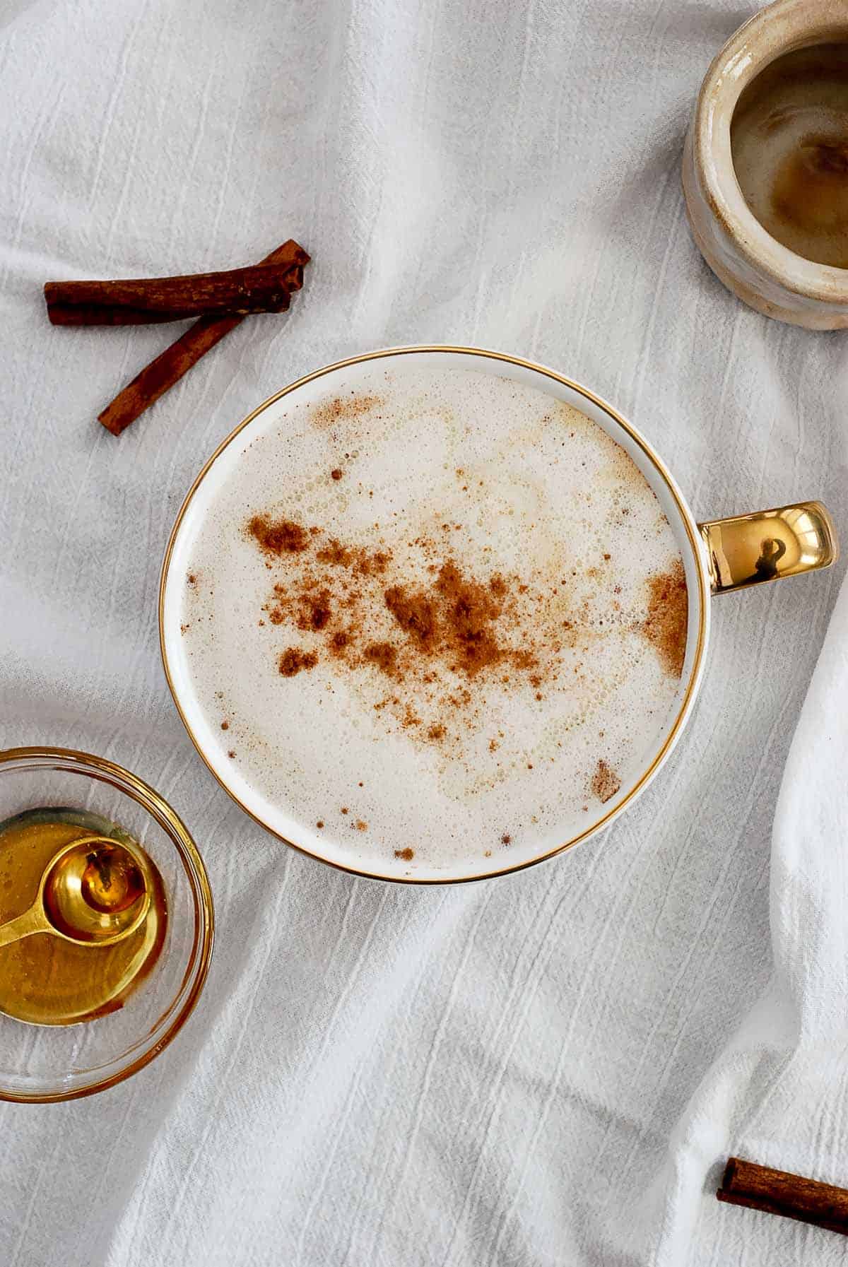 honey latte with cinnamon and honey drizzled on top and bowl of honey on the side.