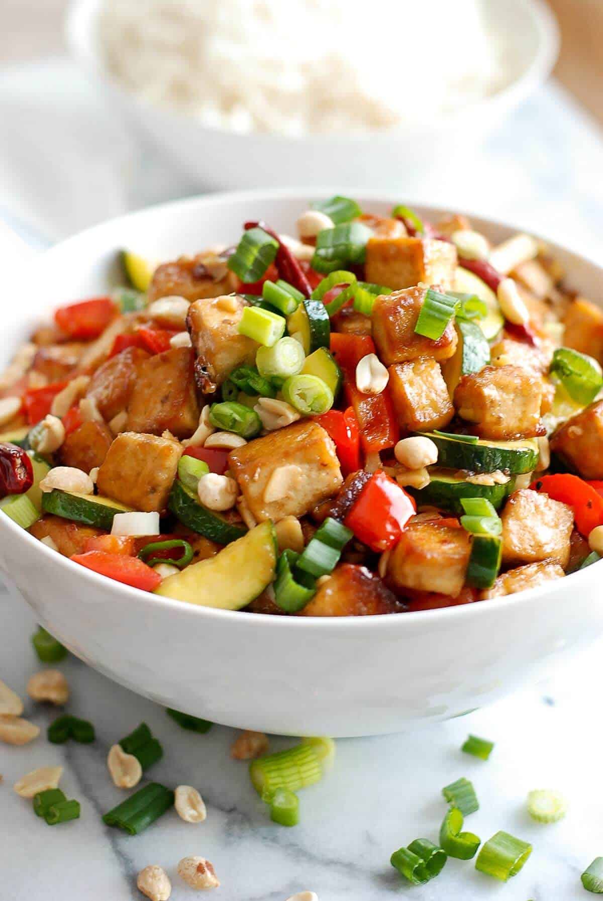 vegetarian kung pao tofu in bowl with rice in the background.