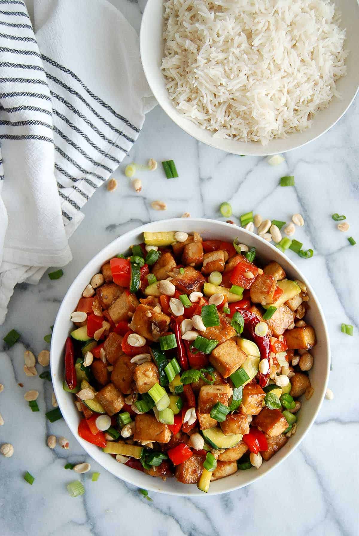 kung pao tofu in bowl in cutting board with rice on the side.