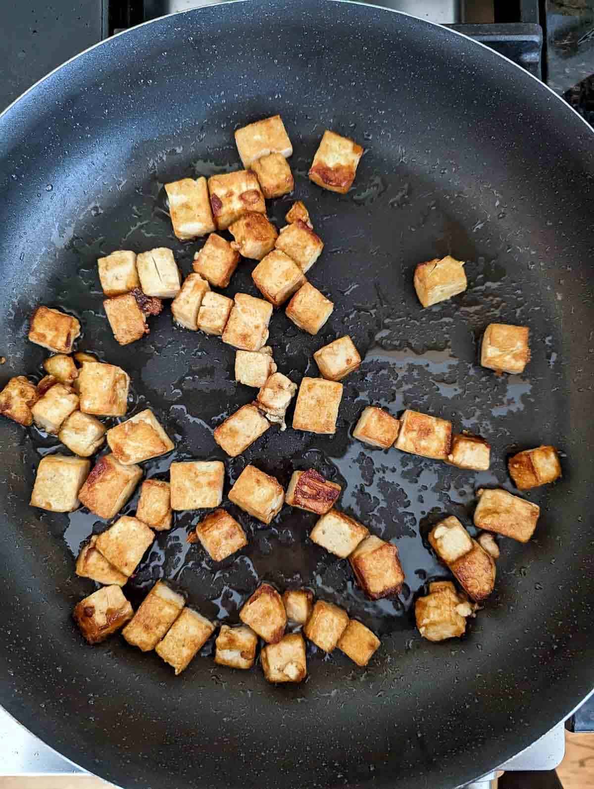 crispy pan fried tofu in pan on stovetop.