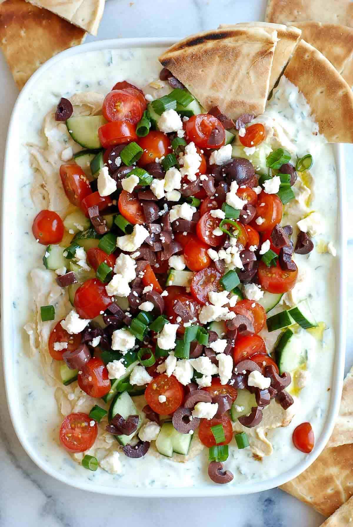 7 layer greek dip on platter with pita bread.