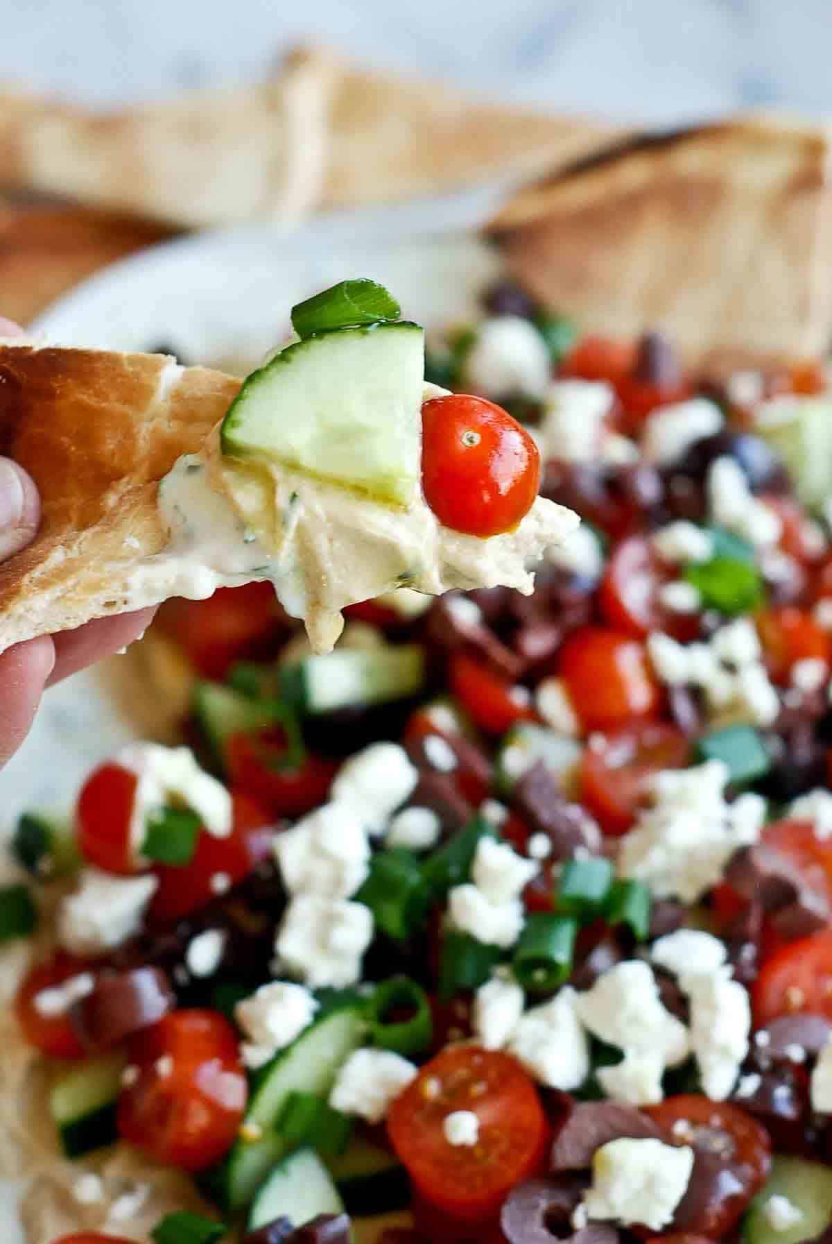 hand holding pita bread with scoop of 7 layer greek dip.