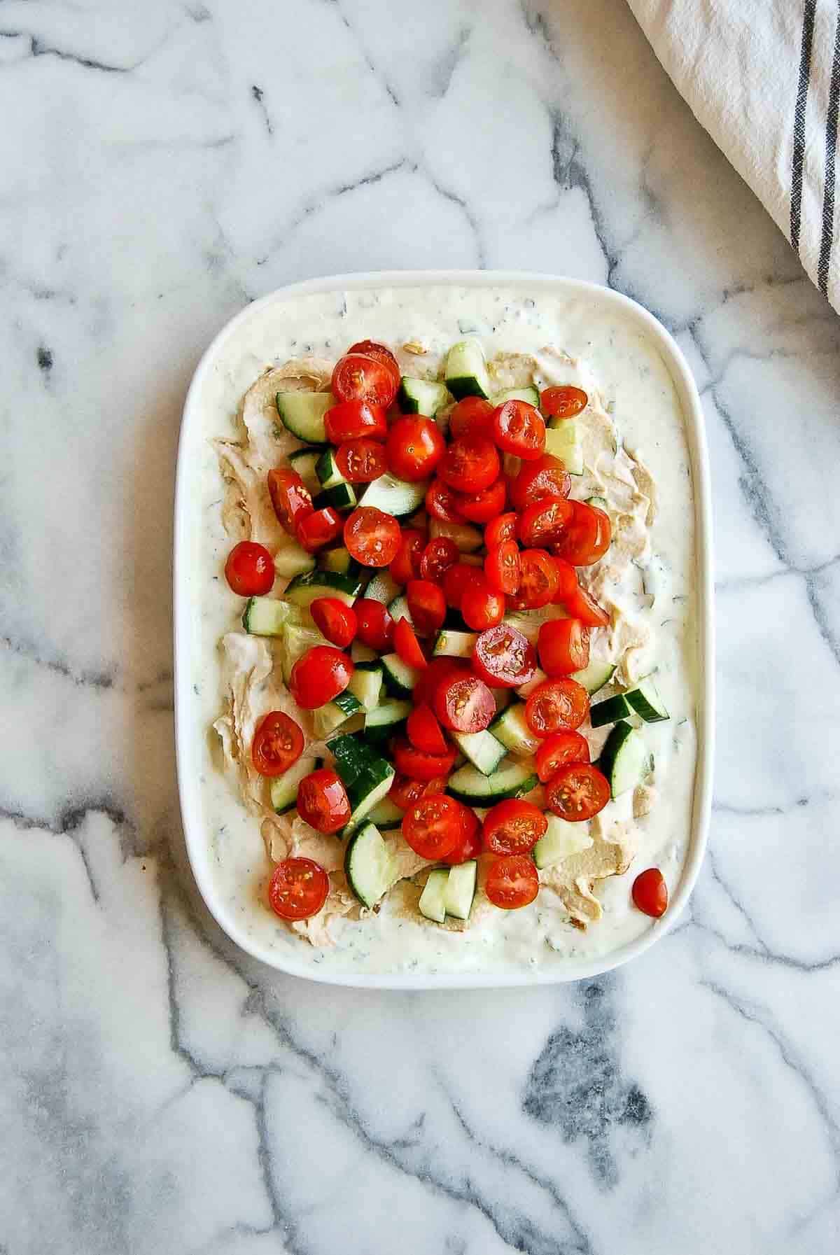 greek yogurt dip, hummus, tomatoes and cucumber on platter.