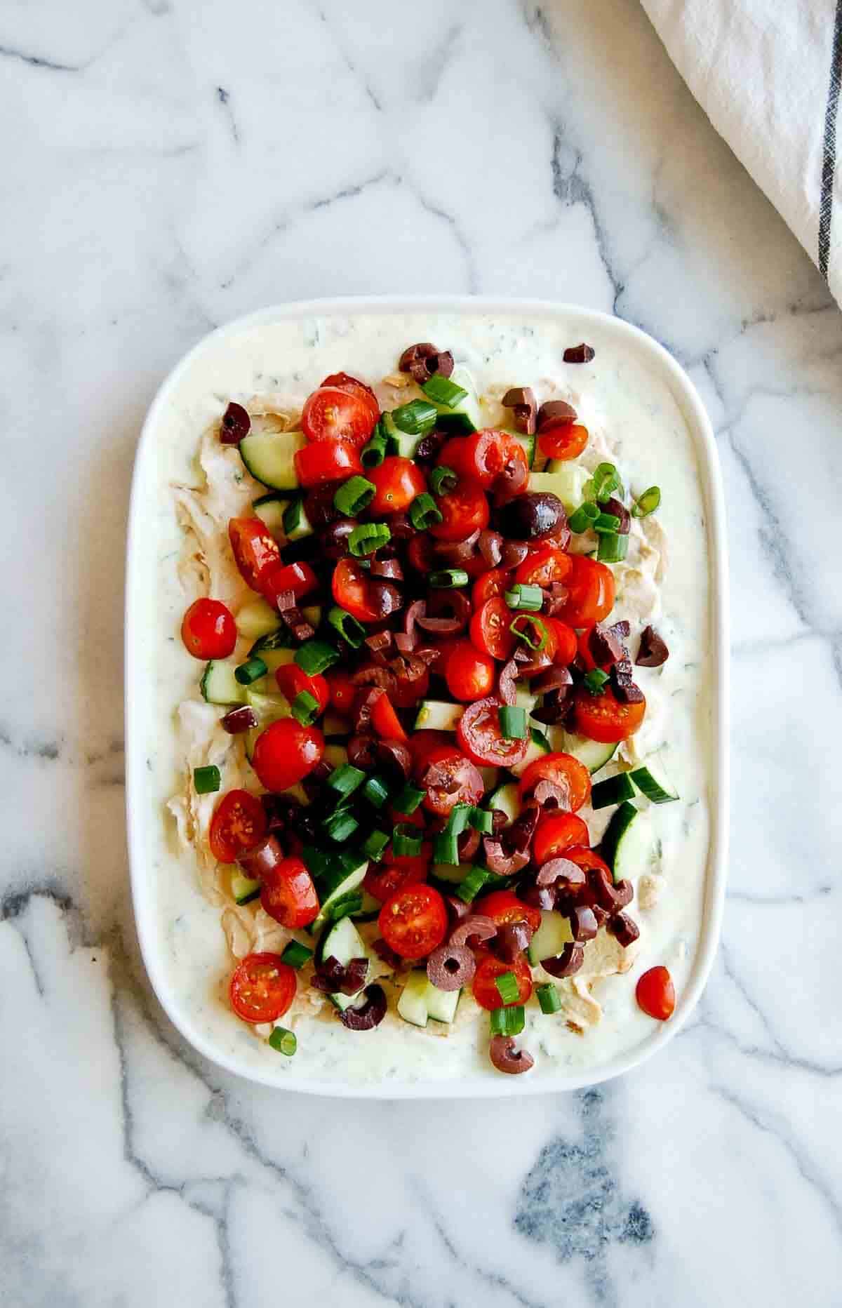 greek yogurt dip, hummus, cucumber tomatoes, scallions and kalamata olives on platter.
