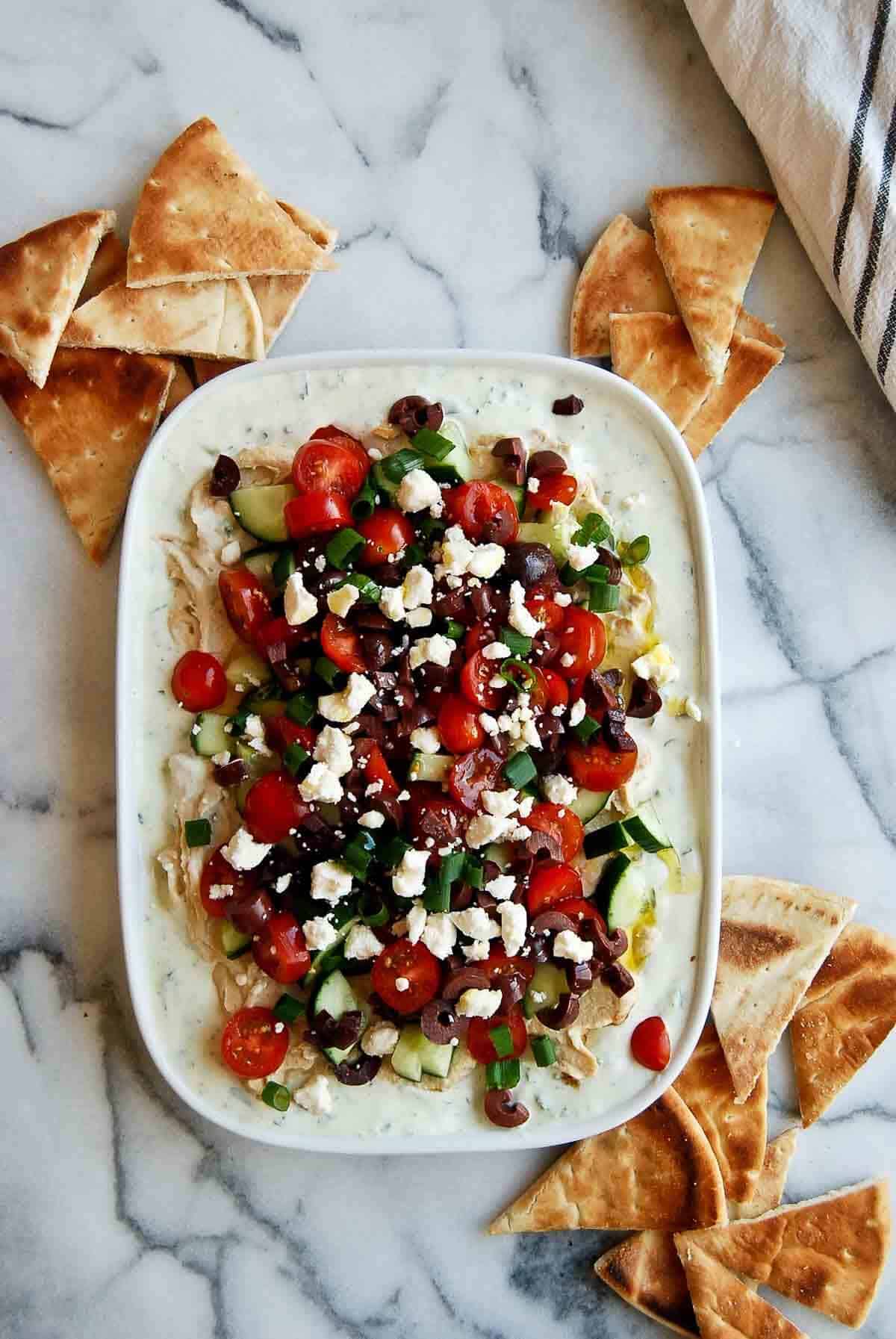 7 layer greek dip on platter with pita triangles scattered around.