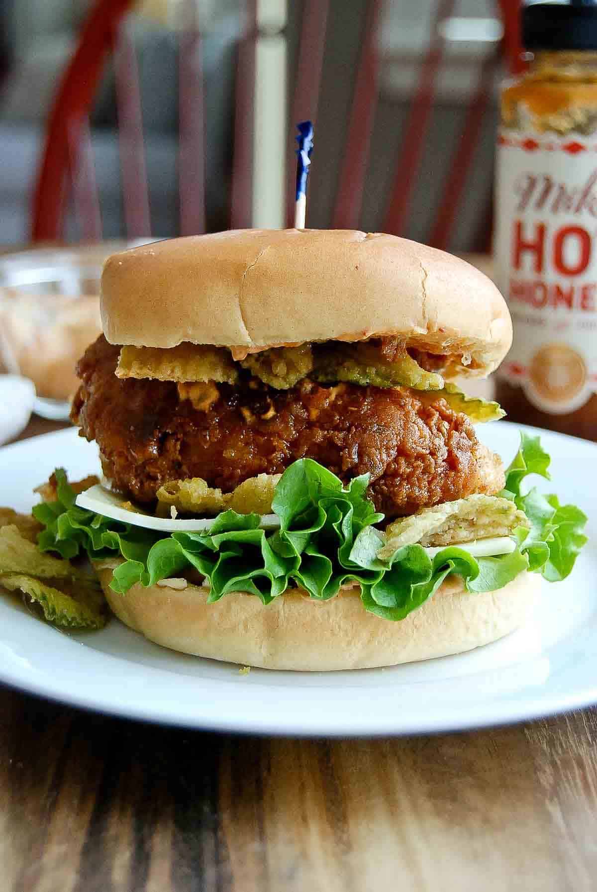 hot honey chicken sandwich on brioche bun on plate with mikes hot honey in the background.