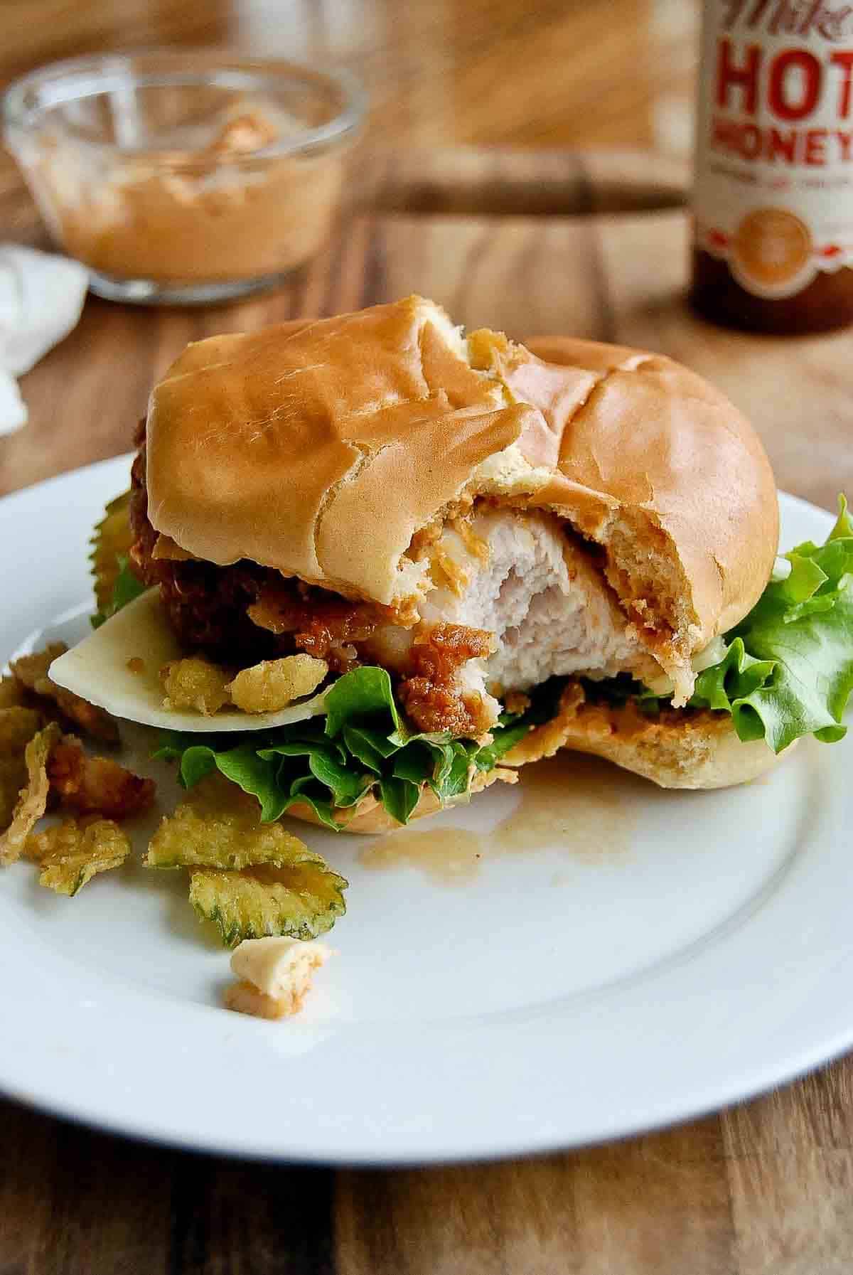 hot honey chicken sandwich with bite taken on plate.