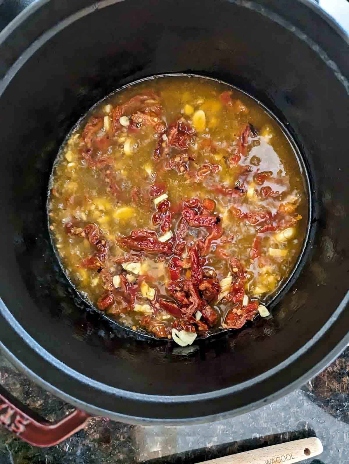 white wine and olive oil garlic sauce with sun dried tomatoes simmering in pot on stove.