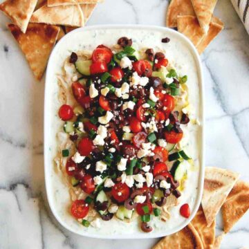 7 layer greek dip on platter with toasted pita bread around it.