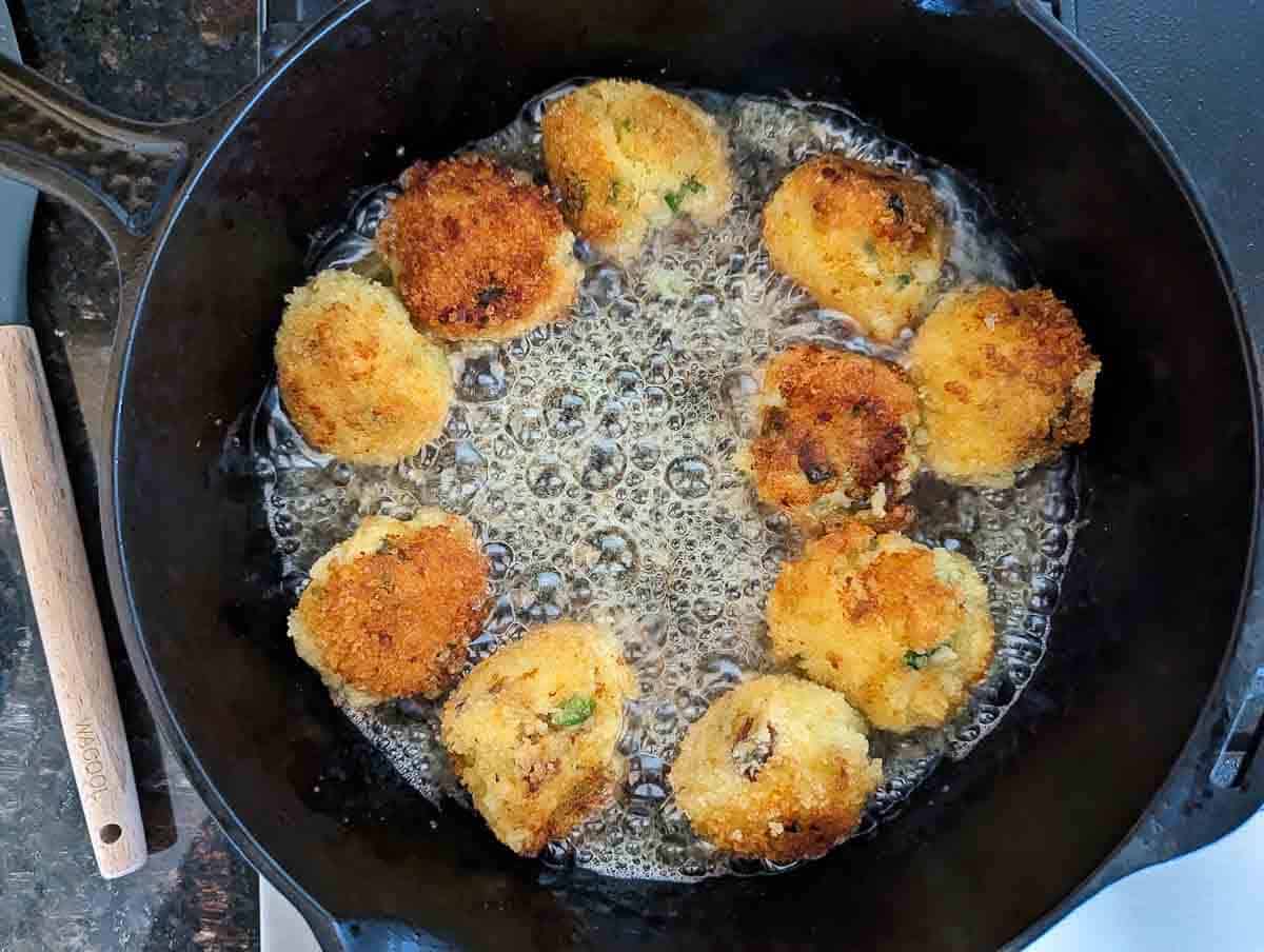 mashed potato balls frying in oil in skillet.