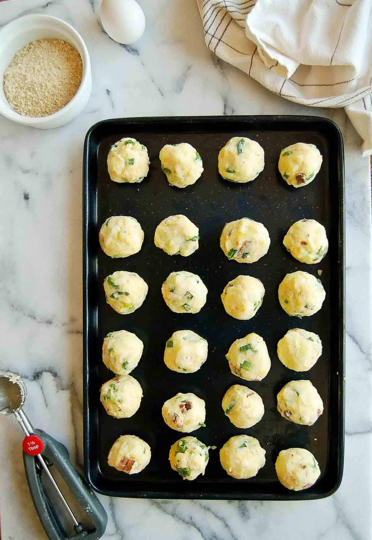 loaded mashed potato balls with bacon cheese and scallions on sheet pan.