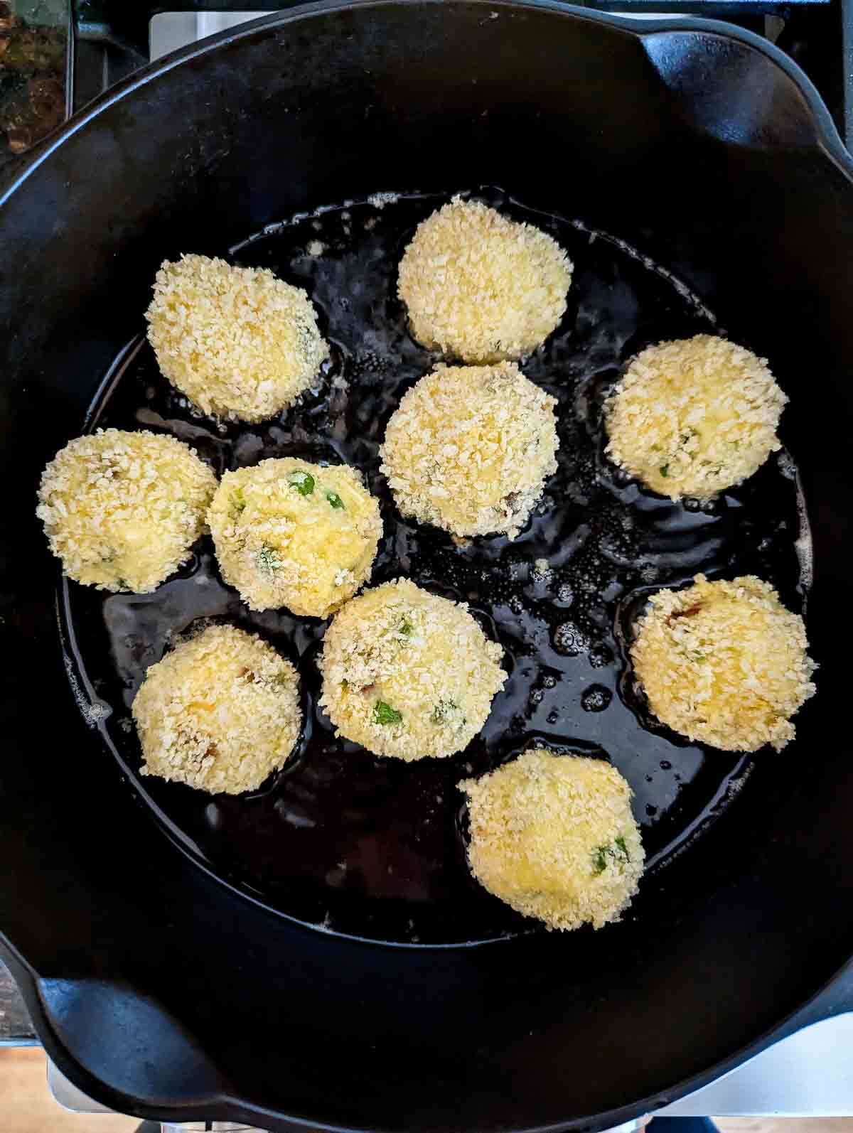 breaded mashed potato balls frying in skillet.